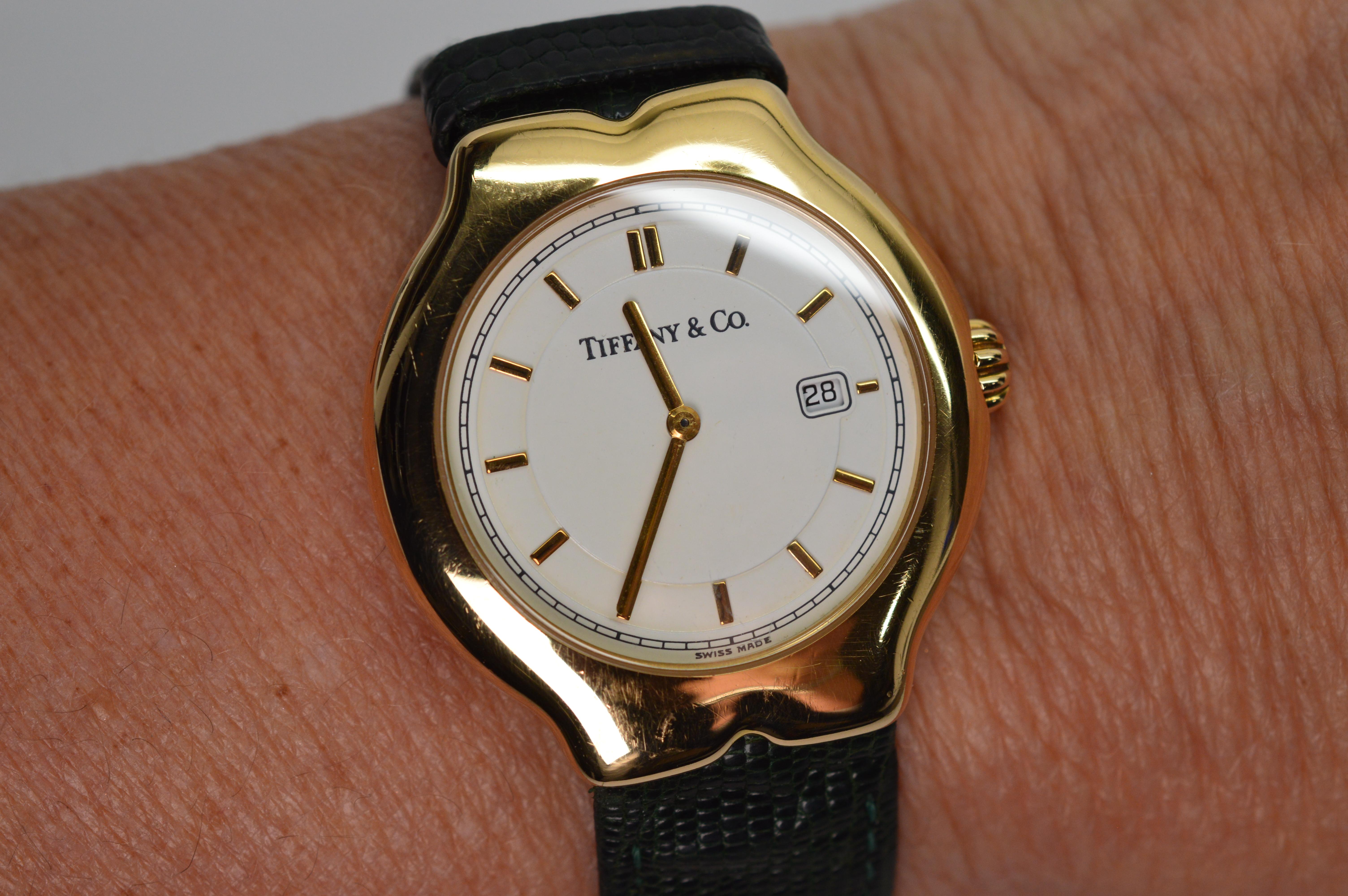 Classic Tiffany and always smart in style. This favorite Tiffany & Co. Tesoro Model Women's Wrist Watch in eighteen karat yellow gold 18K has an easy to read white face with gold match stick numeral markers and date window. Displaying its original