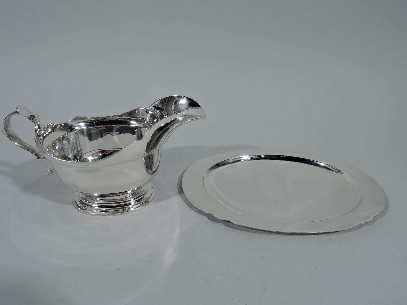 Georgian sterling silver gravy boat. Made by Tiffany & Co. in London in 1936. Traditional form with scalloped helmet mouth, leaf-capped double-scroll handle, and stepped oval foot. Hallmarked. Dimensions: H 3 3/4 x W 7 x D 3 5/8 in. Heavy weight: