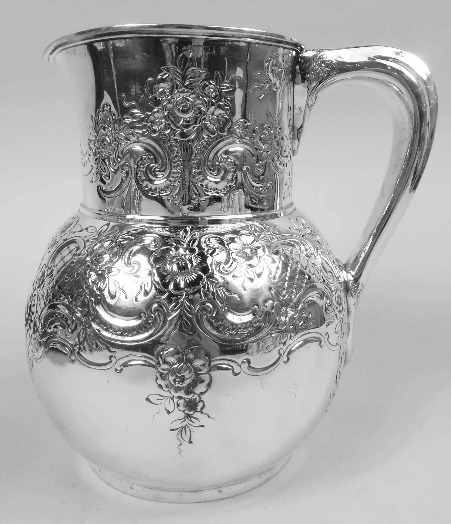 Victorian Classical sterling silver water pitcher. Made by Tiffany & Co. in New York, ca 1878. Globular with drum-form neck, small lip spout, and scroll bracket handle. Chased floral, scroll, and diaper ornament with leafing scrolled frame (vacant).