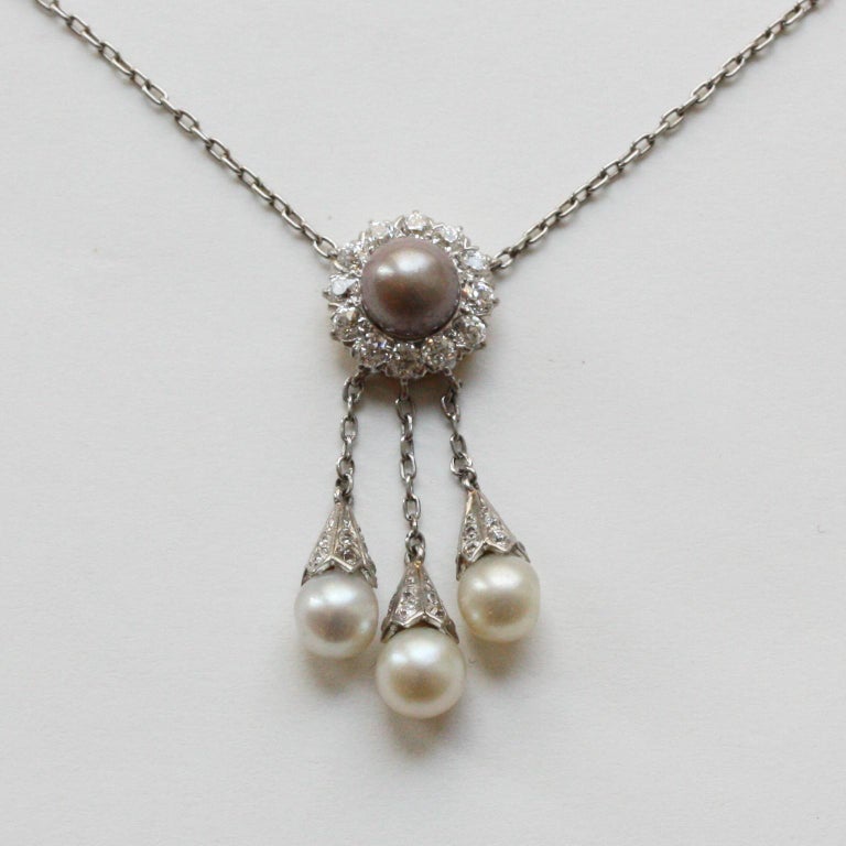 An Edwardian platinum lavalière necklace with a pendant of a flower cluster of a large natural grey pearl surrounded with 12 old cut diamonds underneath are three platinum chains with three natural white pearls, signed: Tiffany & Co., American,