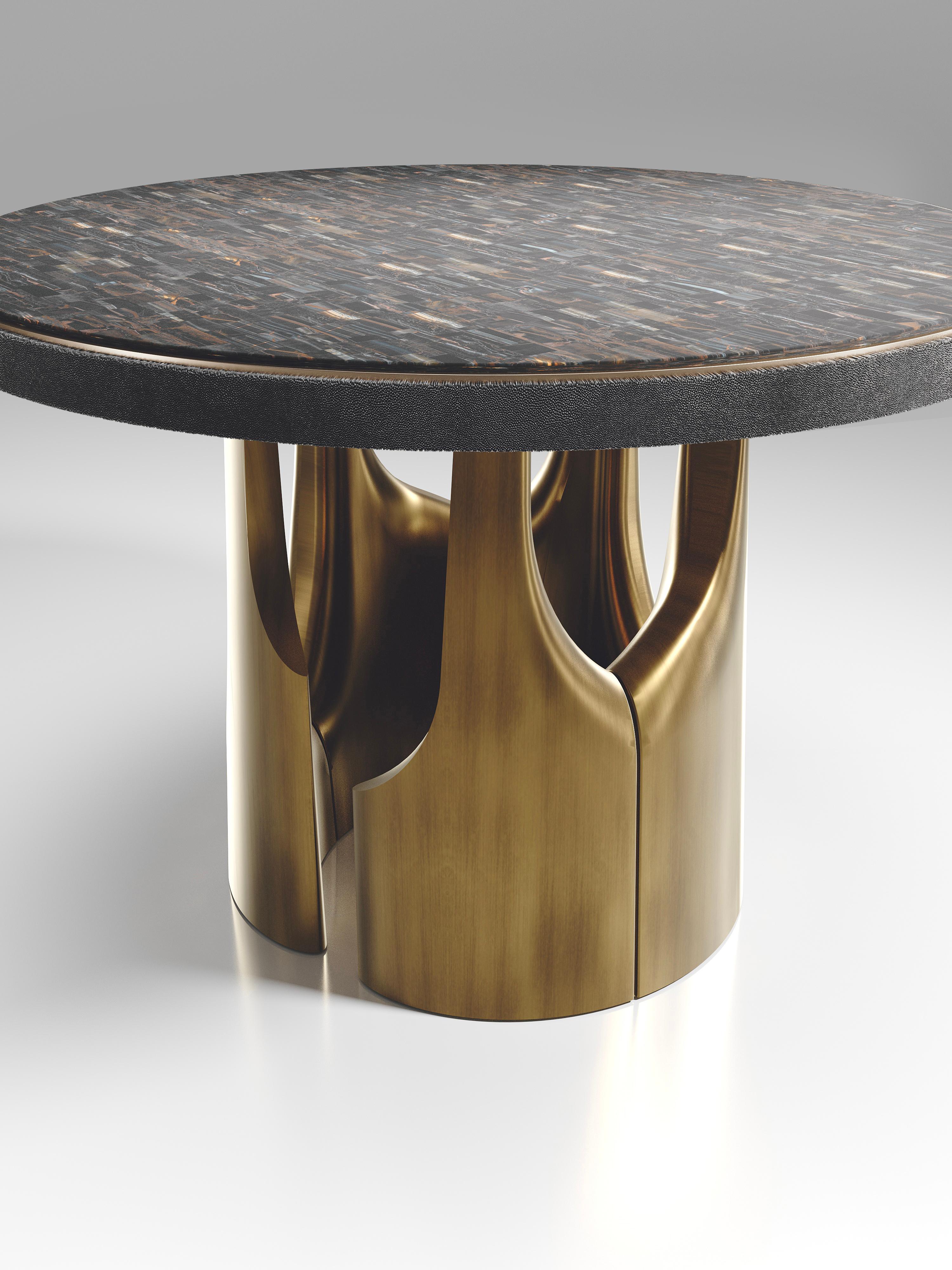 The triptych breakfast table by R&Y Augousti is a stunning multi-faceted sculptural piece. The beautiful hand craved details on the bronze-patina base demonstrate the incredible artisan work of Augousti. The top is in a tiger eye blue with a black