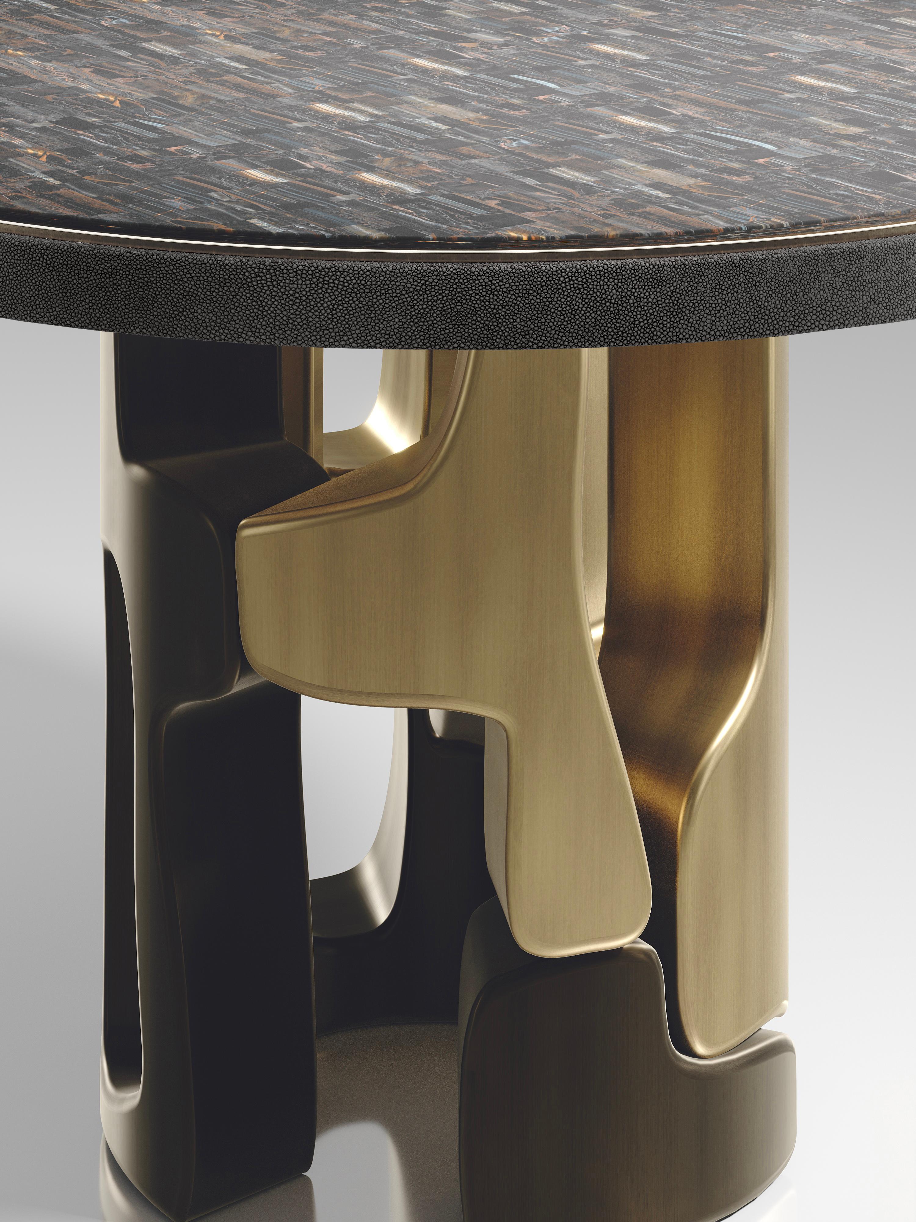 The Apoli breakfast table by Kifu Paris is both dramatic and organic its unique design. The tiger eye blue top sits on an ethereal geometric and sculptural bronze-patina brass base. The side band of the table is inlaid in black shagreen This piece