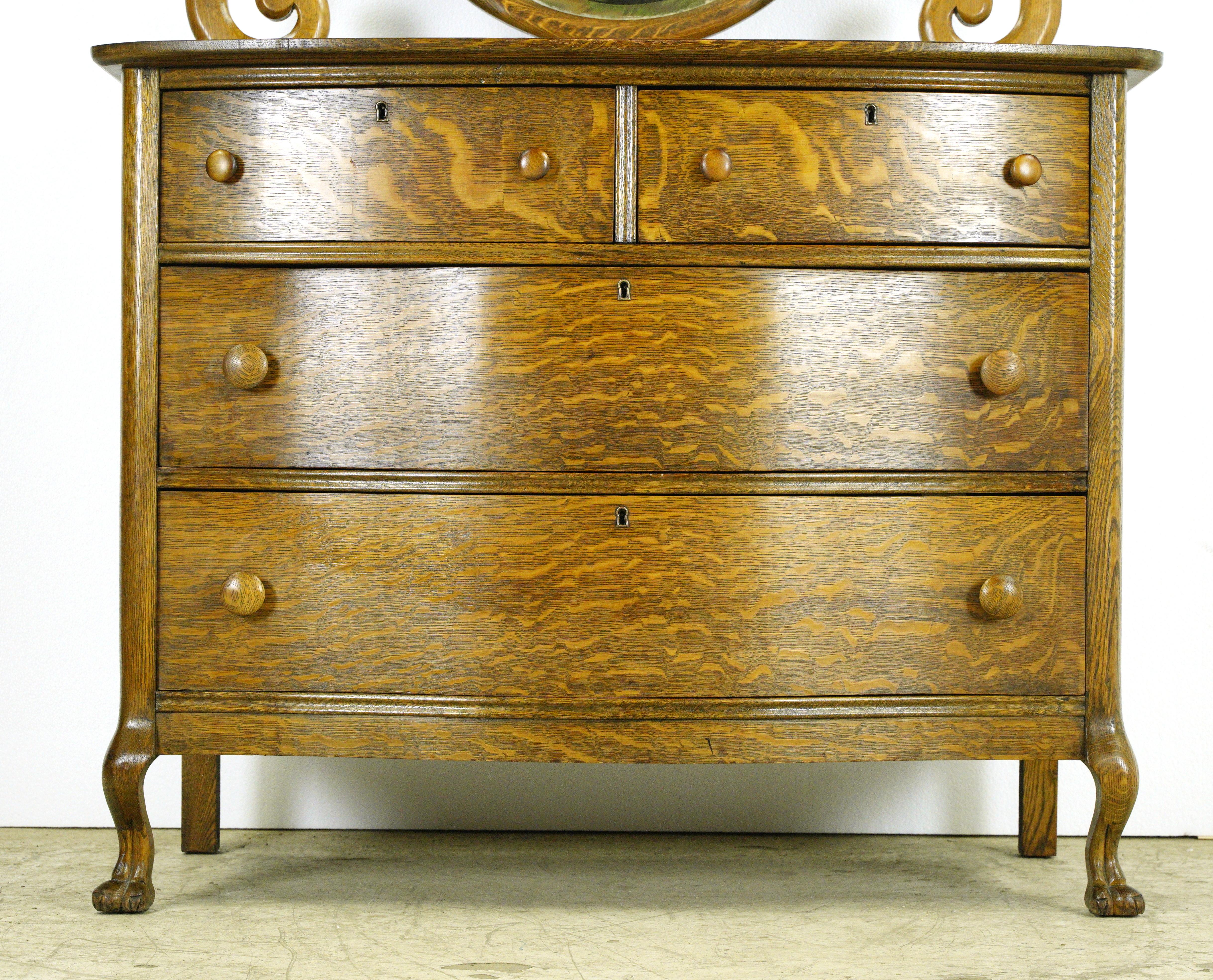 Dark tone antique tiger oak dresser with four dovetailed drawers, a beveled oval mirror and carved claw feet front legs. Good condition with appropriate wear from age. One available. Please note, this item is located in one of our NYC locations.