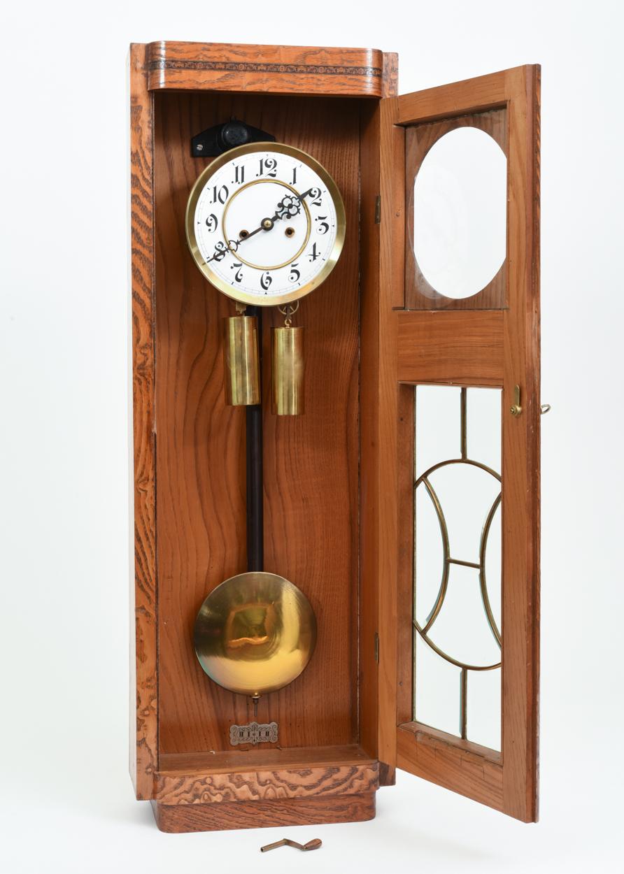 Two weight pendulum Vienna regular hanging clock in tiger oak framed and beveled glass case with trimmed brass details. Eight day time and strike regulator. Gustav stamped movement. The wall clock is in great antique condition with minor wear