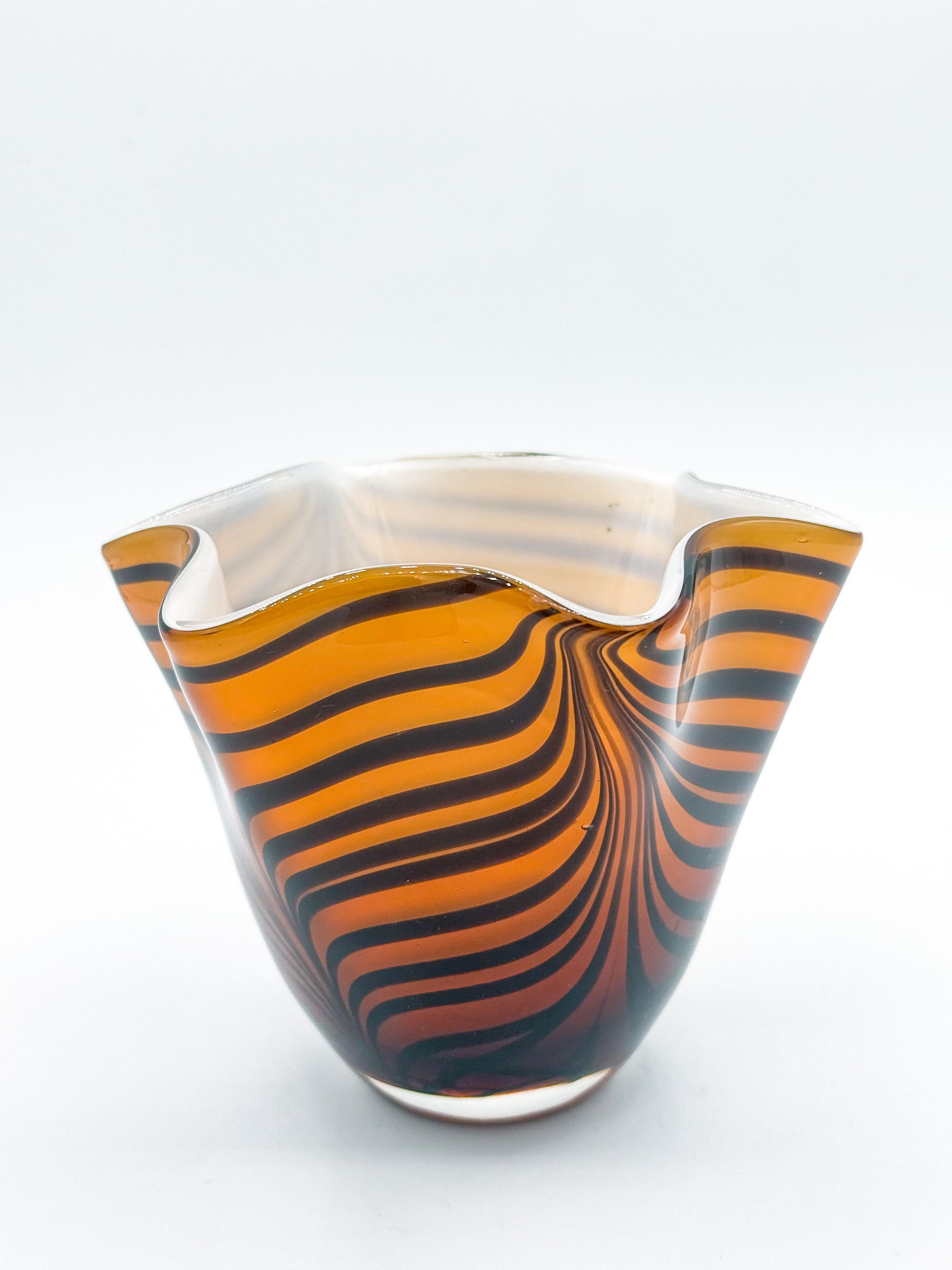 Striking and sculptural, this 1980s Murano art glass vase features a bold tiger stripe pattern in deep amber and black, swirling fluidly across its handblown surface. Crafted in Italy, its ruffled handkerchief form creates a dynamic silhouette that