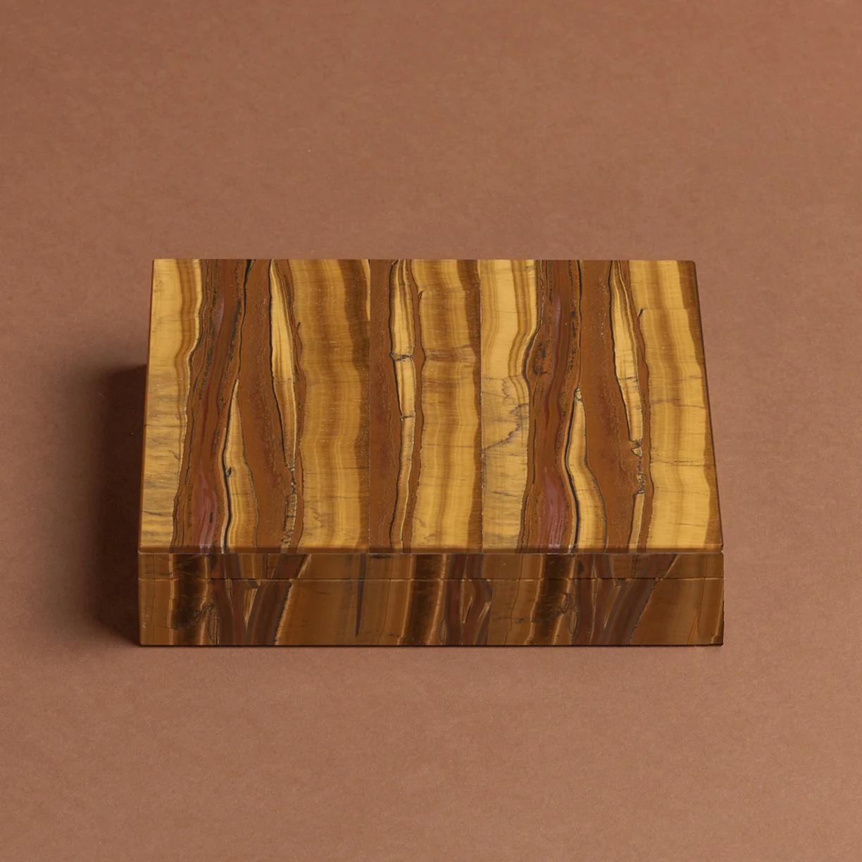 A stylish box made from Tiger's Eye with bands of colour running through the stone. A gilt metal hinge joins the top and bottom sections.

Tiger's Eye is a member of the quartz family of rocks that polishes to a glossy lustre and has a holographic