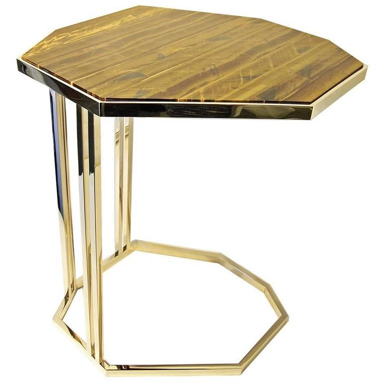 This side table is a rare and one-of-a-kind treasure. A striking octagon shaped, hand-cut piece of Tiger's eye, known for its chatoyant appearance, sits atop a luxurious handcrafted brass base with a light gold finish. The base bares a unique 'C'