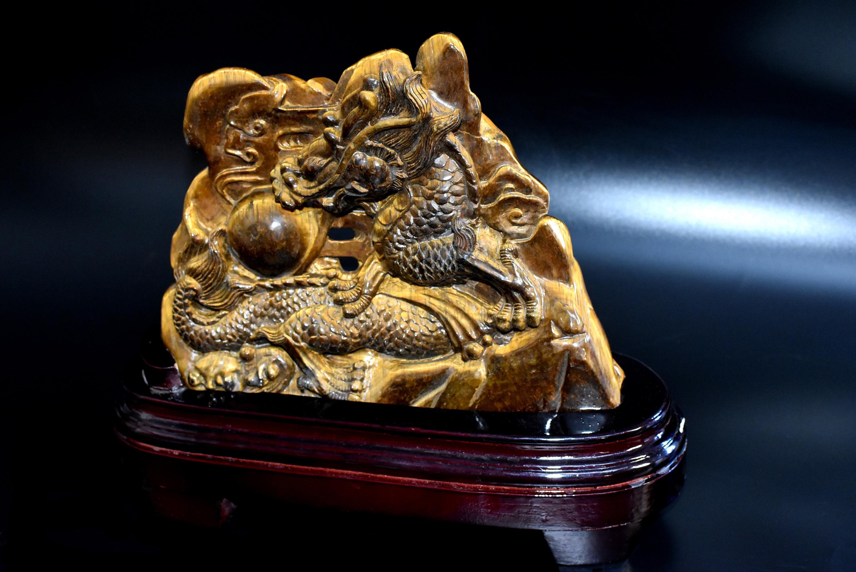 A stunning hand carved 2.2 lb tiger's eye sculpture depicting dragon chasing a pearl in the late Qing dynasty style. The four-clawed dragon under the auspicious clouds has one front talon below its subject, a flaming pearl, while the other three are