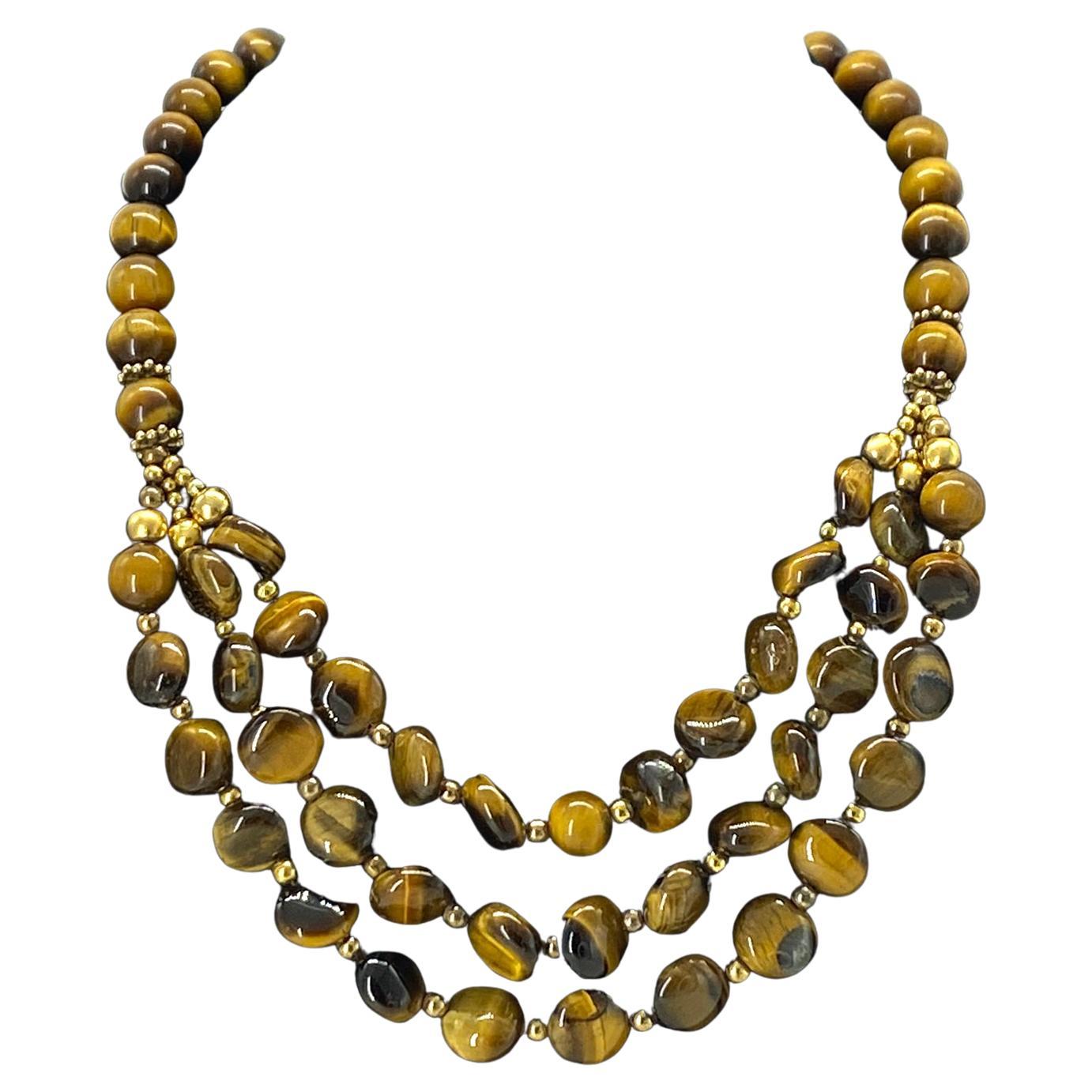 Questa è una collana a più fili con gemma Occhio di Tigre. È un'opera originale di Nouveau Boutique. Ci sono tre fili di perline a forma di bottone da 12-14 mm come pettorale e perline rotonde da 10 mm per il resto della collana. È dotata di una