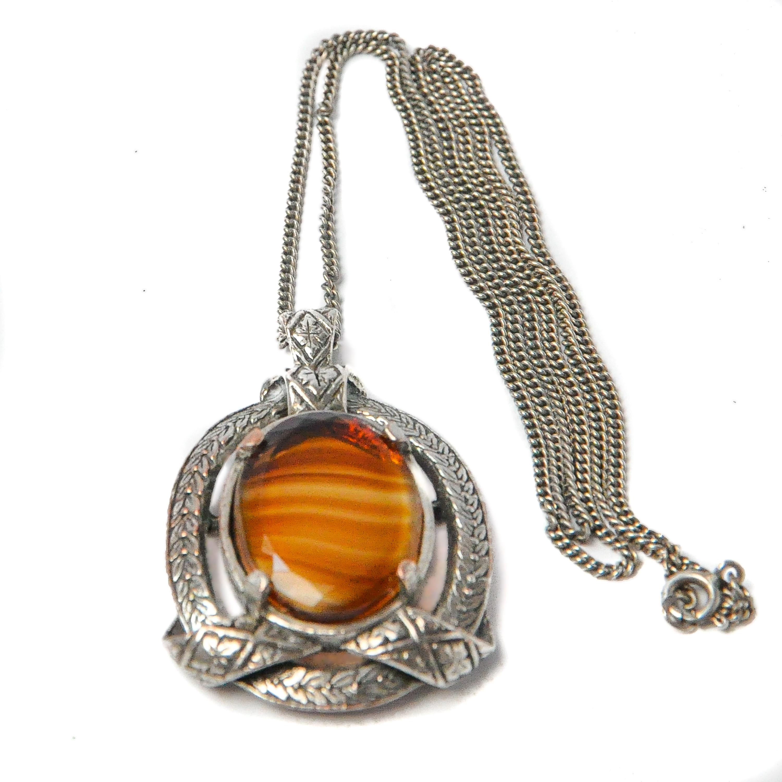 This beautiful vintage pendant necklace is set with a large tiger's eye quartz stone. The silver frame has nice engraved details with a floral decor. The border of the silver frame has a wreath-like design. The tiger's eye is oval-shaped and has a