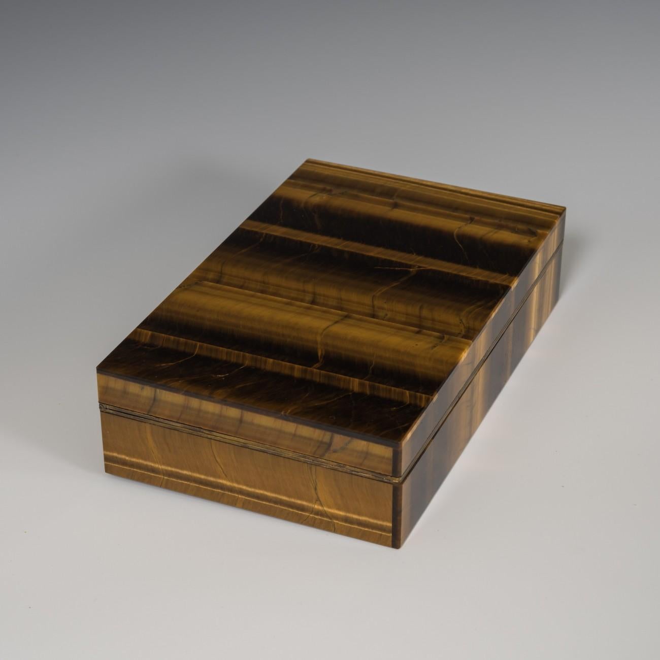 A stylish box made from tiger's eye with bands of brown and gold color running through the stone. Originally used as a cigarette box, a silver gilt hinge and frame join the top and bottom sections. Stamped with the Italian silver mark for 800