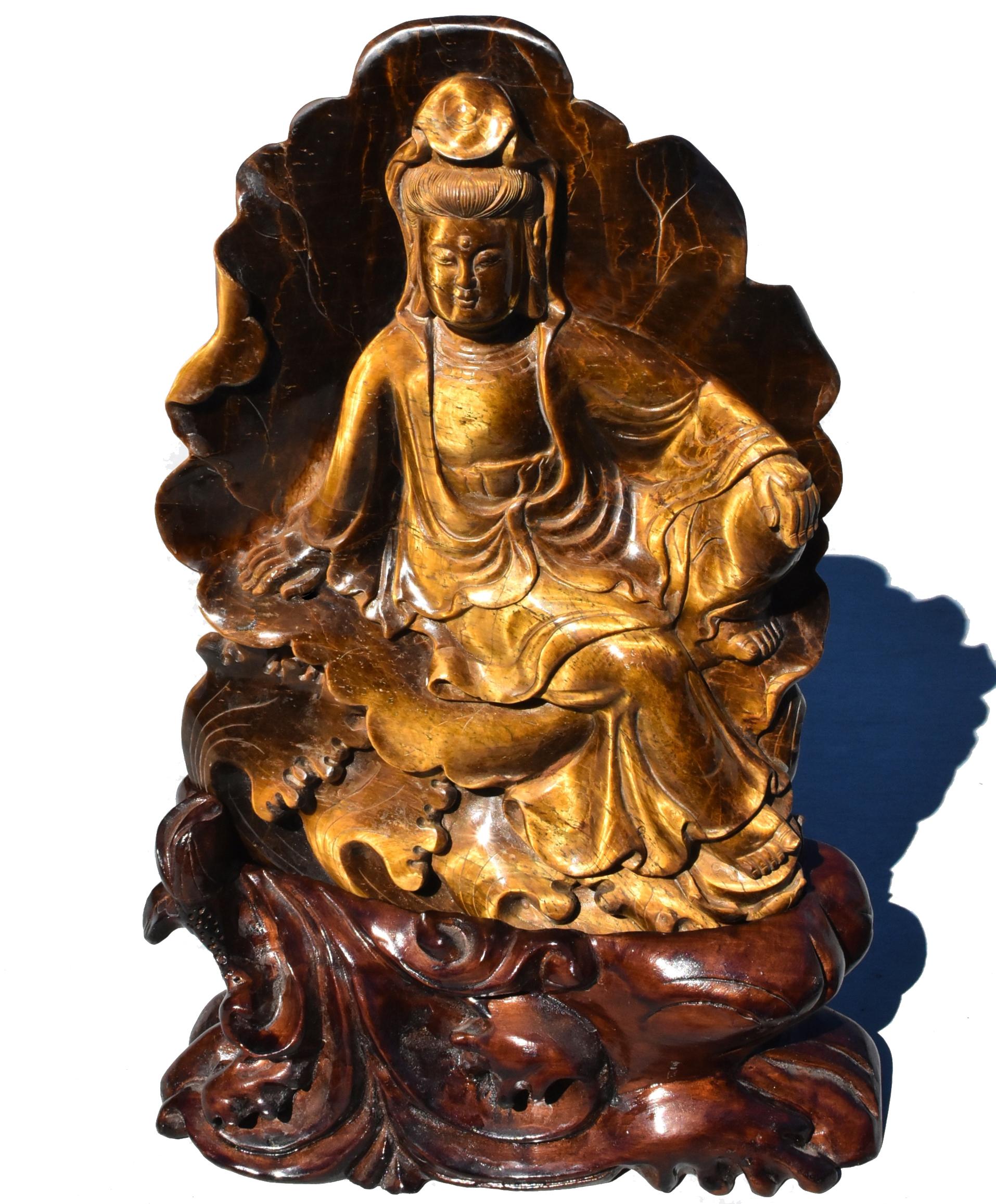 Une magnifique sculpture naturelle en œil de tigre représentant le bodhisattva compatissant Lune d'eau Guan Yin, Avalokiteshvara. Soutenu par une feuille de lotus et surmonté de vagues d'eau, Avalokiteshvara est représenté assis en rajalilasana, la