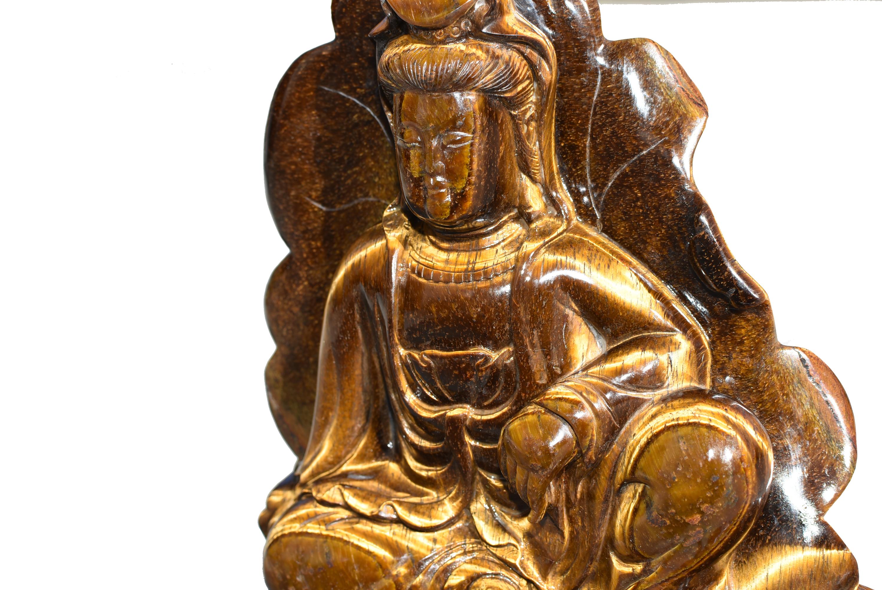 A magnificent natural Tiger's Eye sculpture depicting the compassionate Bodhisattva Water Moon Guan Yin, Avalokiteshvara. Seated on a lotus base in rajalilasana, the ‘posture of royal ease’, backed by a lotus leaf, Avalokiteshvara wears a hooded