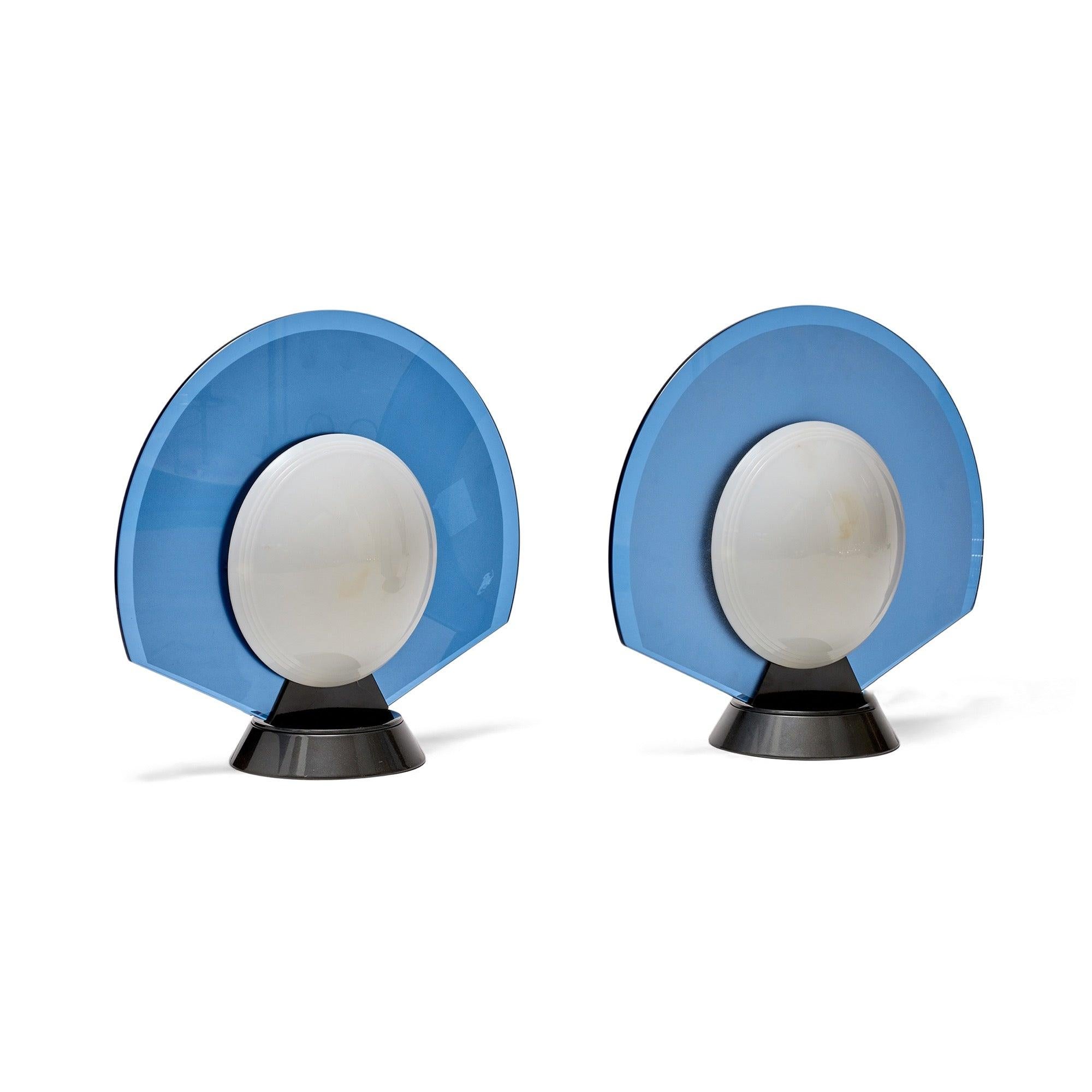 A dramatic and geometric pair of table lamps in translucent blue glass with attached white plastic diffusers perched atop a weighted and swiveling conical steel base. ?