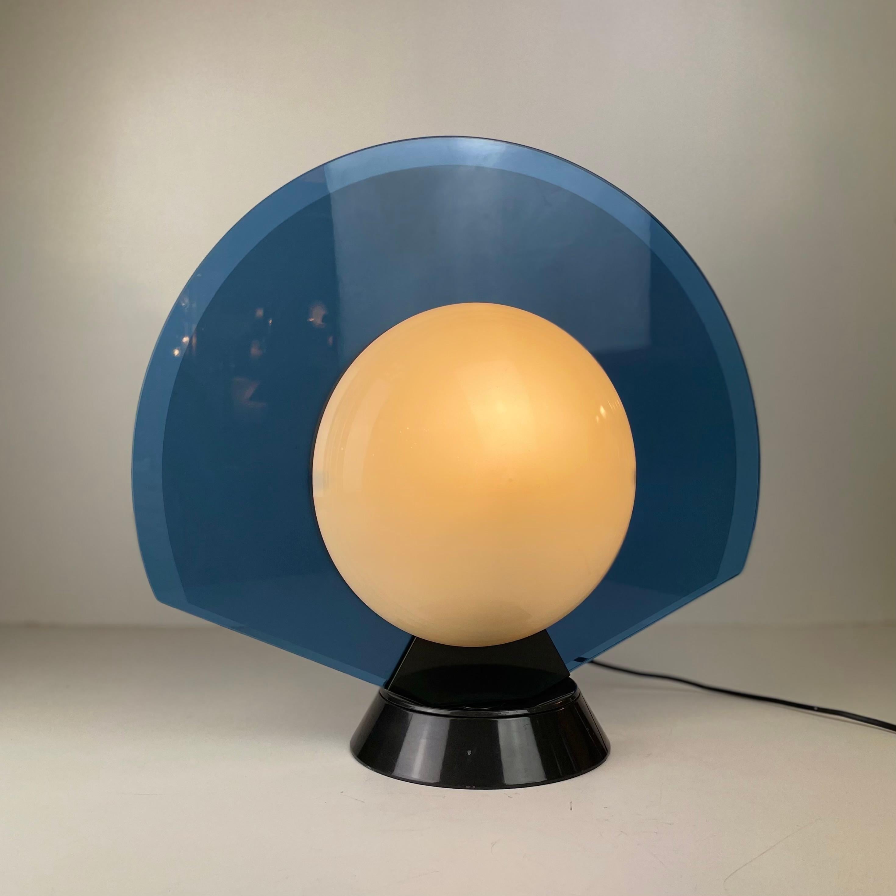 Postmodern table lamp made of a swiveling blue glass disc with an white acrylic lampshade a black round base, designed by Pier Giuseppe Ramella for Arteluce in the 1980’s.
-
Lampe de table postmoderne composée d'un disque en verre bleu pivotant avec