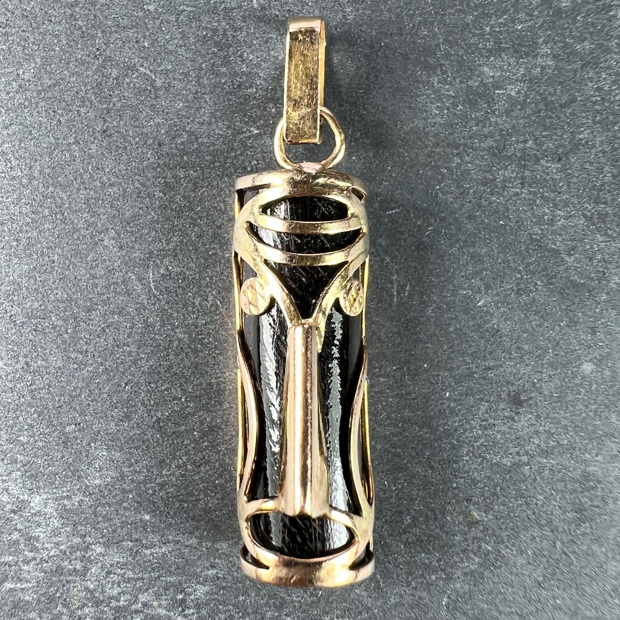 Un ciondolo portafortuna in oro rosa e legno scuro (14K) disegnato come una maschera hawaiana o maori Tiki in filo d'oro rosa su un mezzo cilindro di legno scuro per l'aspetto portafortuna del tema Touch Wood. Non marcato ma testato per l'oro a 14