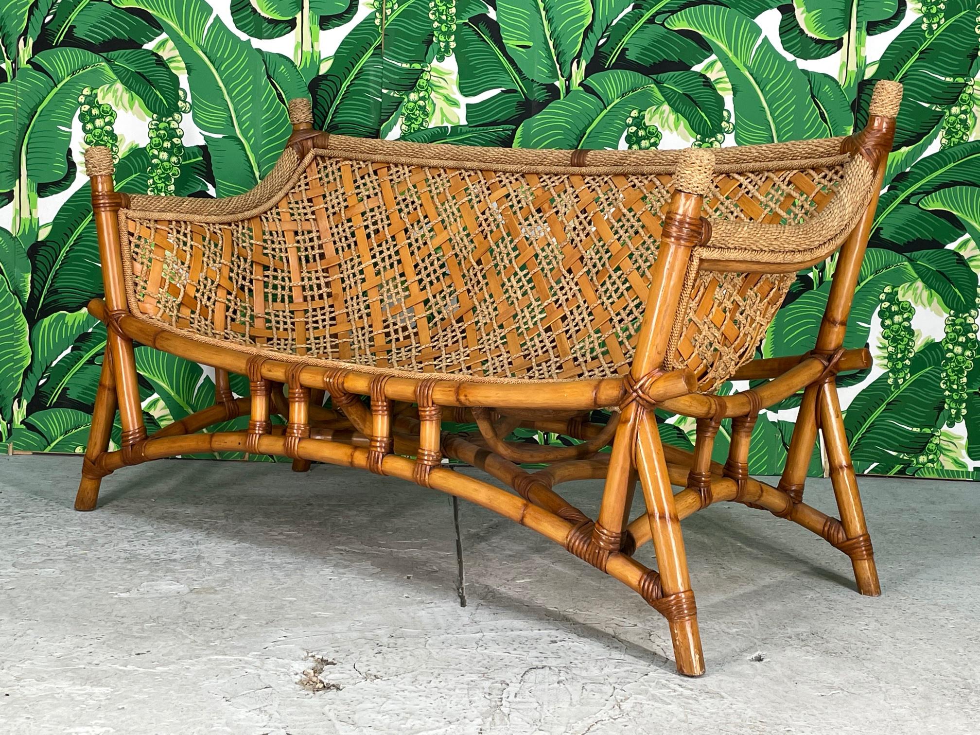 Unique vintage rattan bench sofa features a sling seat design and woven rope and reed detailing. Chinoiserie influence with it's pagoda style base and flared legs. Good condition with imperfections consistent with age, see photos for condition