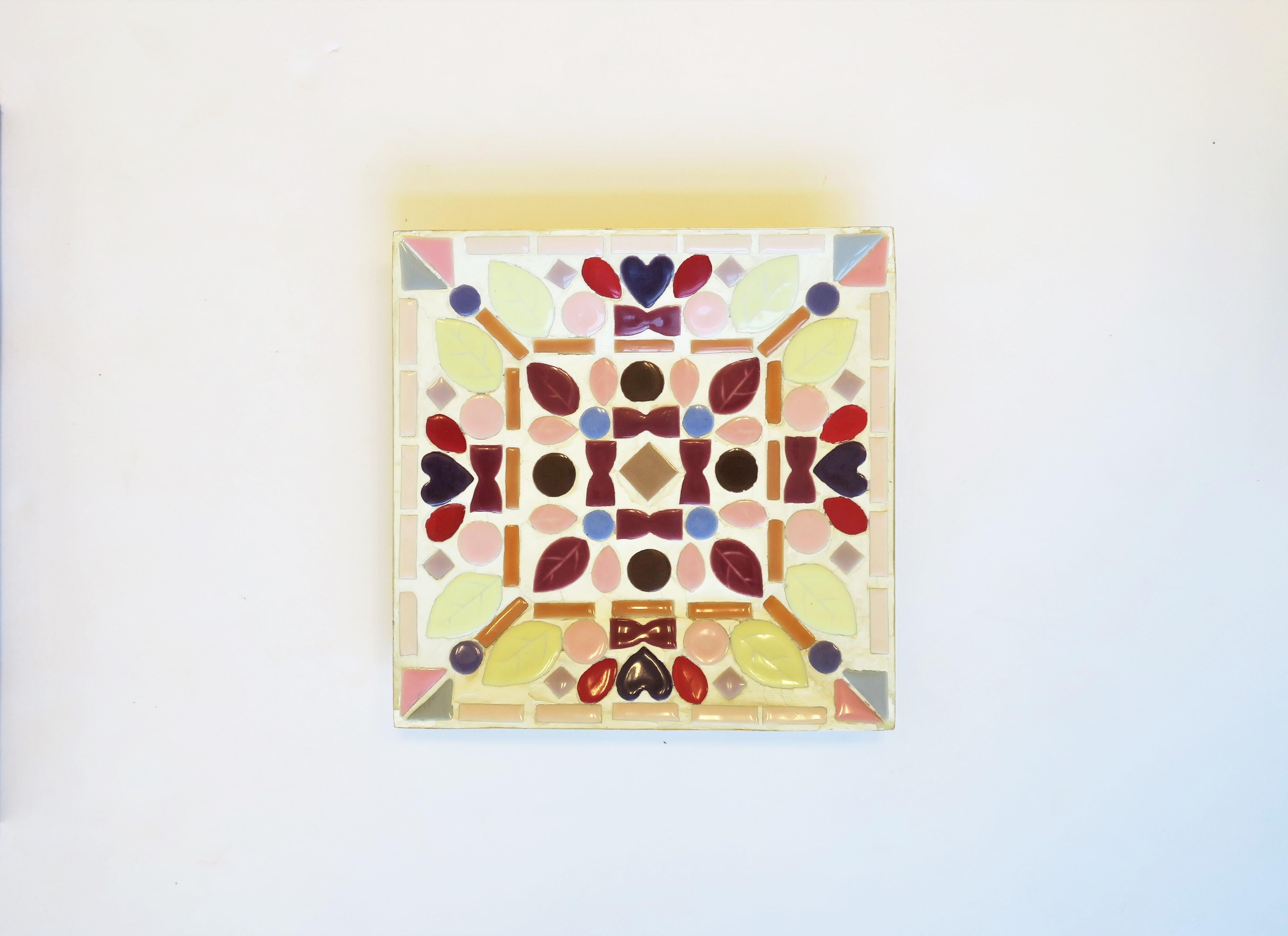 A very beautiful tile mosaic dish bowl vide-poche, circa 1960s-1970s, USA. Dish is square; designed with geometric tiles along with tiles in heart, leaf and teardrop shapes. Tile colors include pastel yellow, pinks, and purples, together with rich