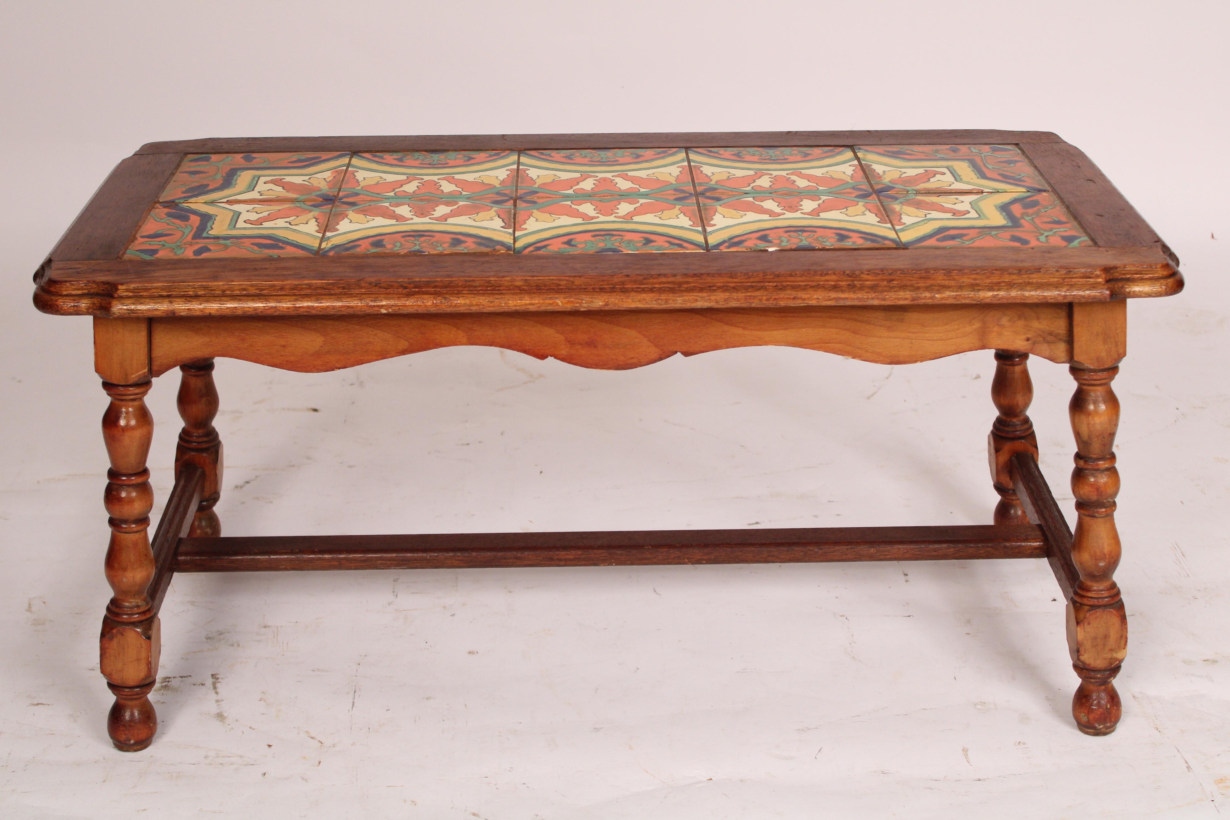 Spanish style oak coffee table with a tile top, circa 1930's. The top with an oak overhanging top inset with 10 colorful tiles, a scalloped apron, turned oak legs joined by an H shaped stretcher bar.