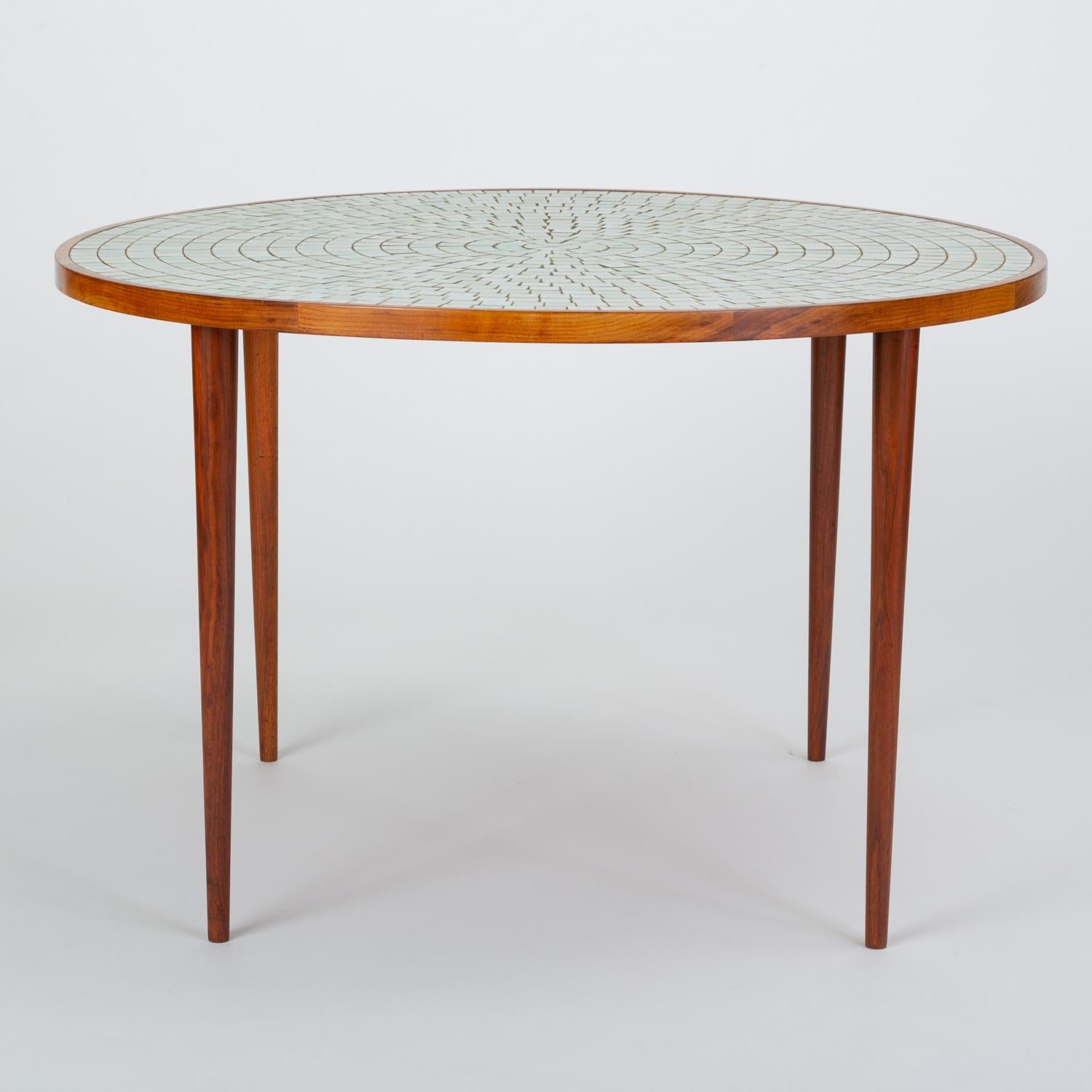 A round dining table from designer husband-and-wife team, Gordon and Jane Martz for their family company Marshal Studios. The table has a walnut frame and tapered dowel legs in matching walnut. The tabletop is inlaid with white ceramic tiles that