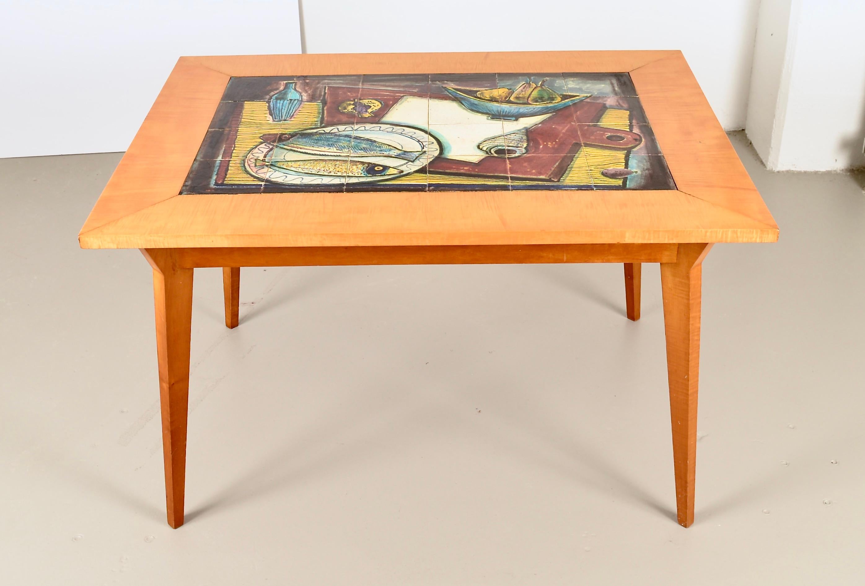 Handsome tile top table, made in France, circa 1950s. Wood base is tiger maple, in a soft satin finish. The colorful tiles are likely made in Biot, France and show a still life featuring fish and fruit. Beautifully made and in excellent condition.