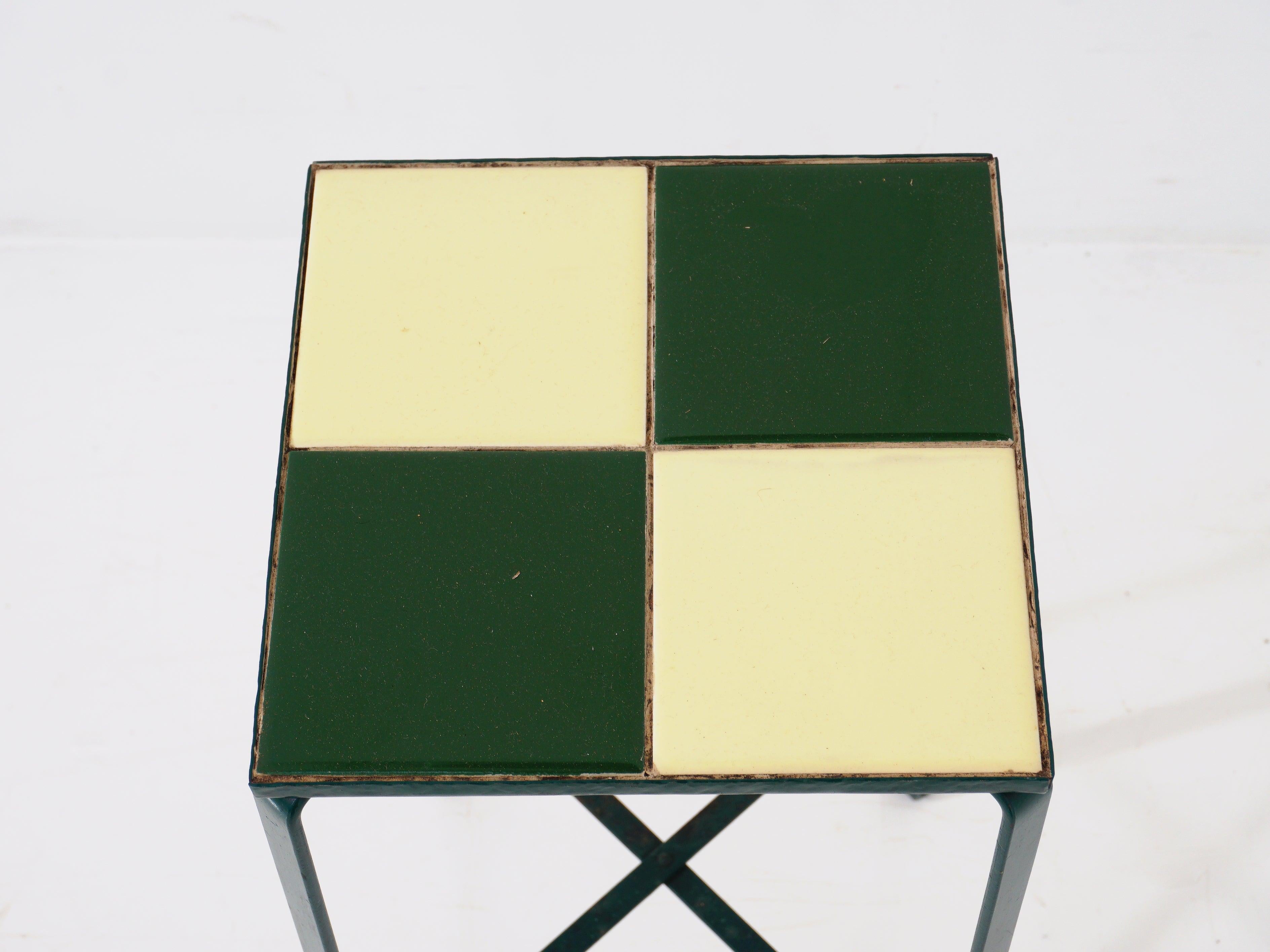 Experience the epitome of midcentury chic with this petite accent table. Featuring a striking tile top that exudes vintage charm, paired with a sleek, green wrought iron base for a pop of personality. This table effortlessly marries form and