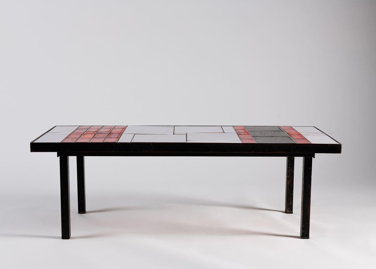 An elegant rectangular coffee table with a pared down dark metal frame and a tiled top arranged in a Mondrianesque pattern of black, red, and white rhombuses. 

 