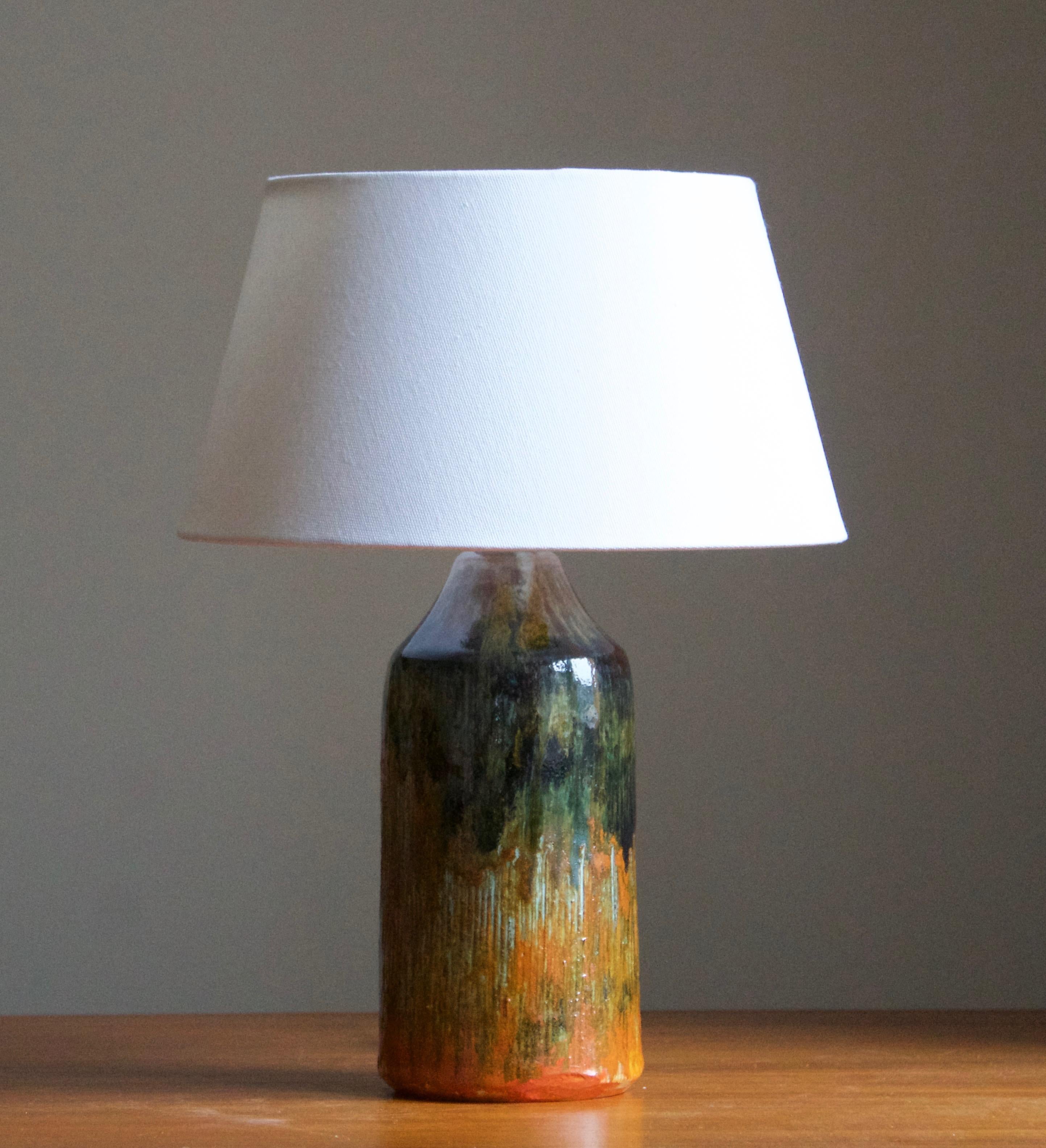 A glazed stoneware table lamp. By Tilgmans Keramik, 1950s. Features a complex glaze combined with incised decor in a style iconic to the producer. Features green, blue orange and red tones.

Stated dimensions exclude lampshade. Height includes