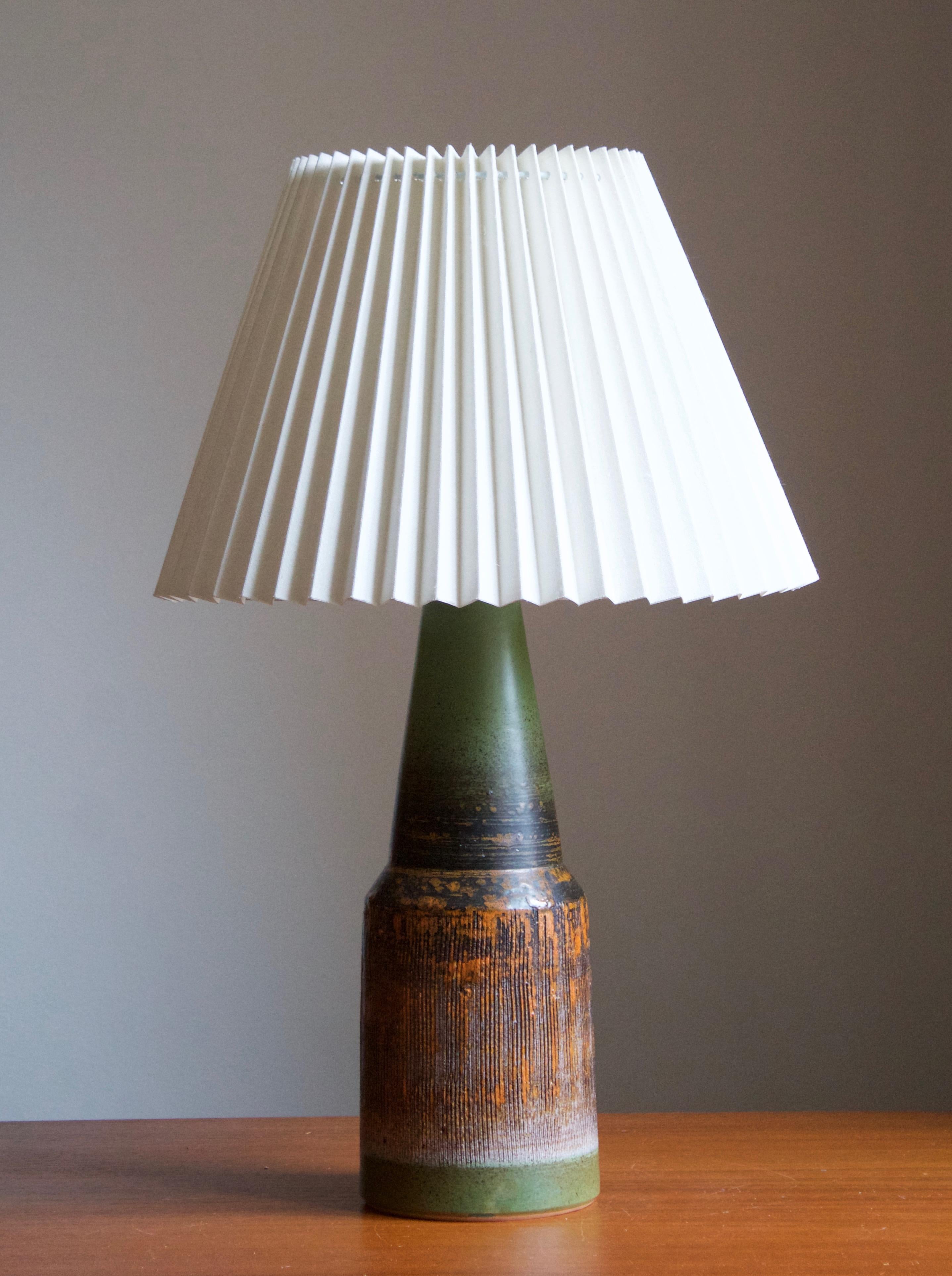 A sizable glazed stoneware table lamp. By Tilgmans Keramik, 1950s. Features a complex glaze combined with incised decor in a style iconic to the producer. Features green, orange and red tones.

Stated dimensions exclude lampshade. Height includes