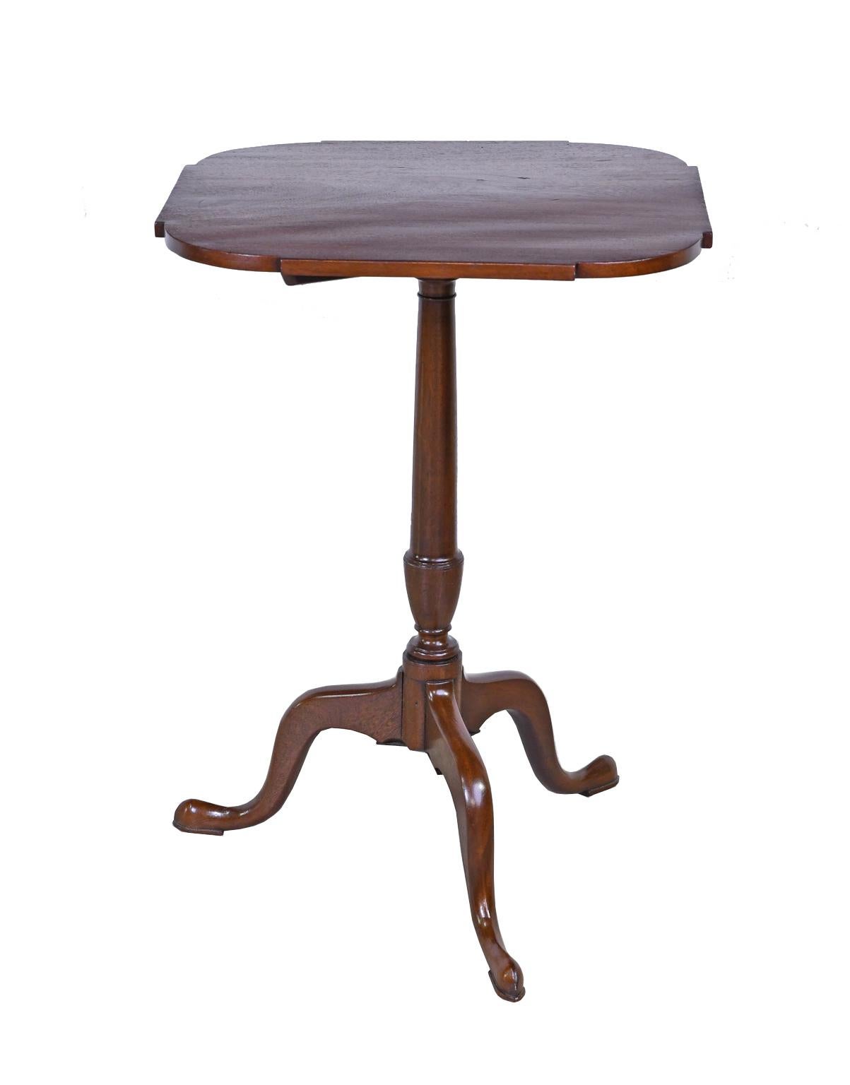 In the style of Thomas Chippendale, a lovely American 18th century tilt-top table in mahogany that, historically, doubled as a candlestand. The square top is cut in curves at the corners and rests on a tripod pedestal whose column ends in a vase