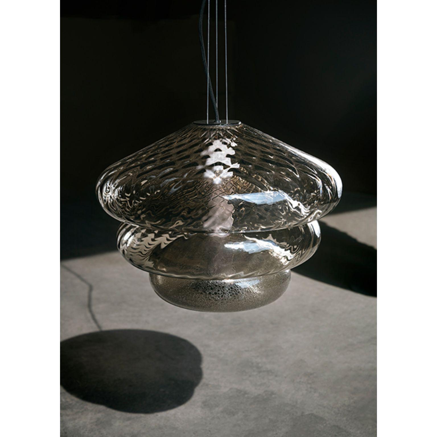 Tima pendant light by Luca Nichetto
Materials: Shade: Clear/Grigio Kaiser/Amber mouth blown glass
 Structure: Bronze satin, black chrome and glass
Dimensions: W 44.2 x D 44.2 x H 34 cm

Customization available.

In the roundness of their