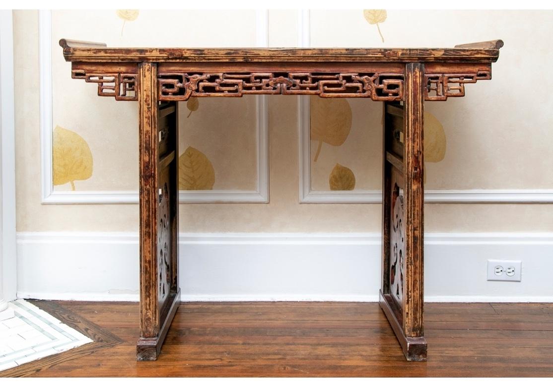 A more diminutive Asian Wood Altar table with some of the original oxblood tone paint preserved. With a plank constructed banded top with upcurved ends. An openwork geometric frieze on the front, and a shaped flat one at the back. Elaborate