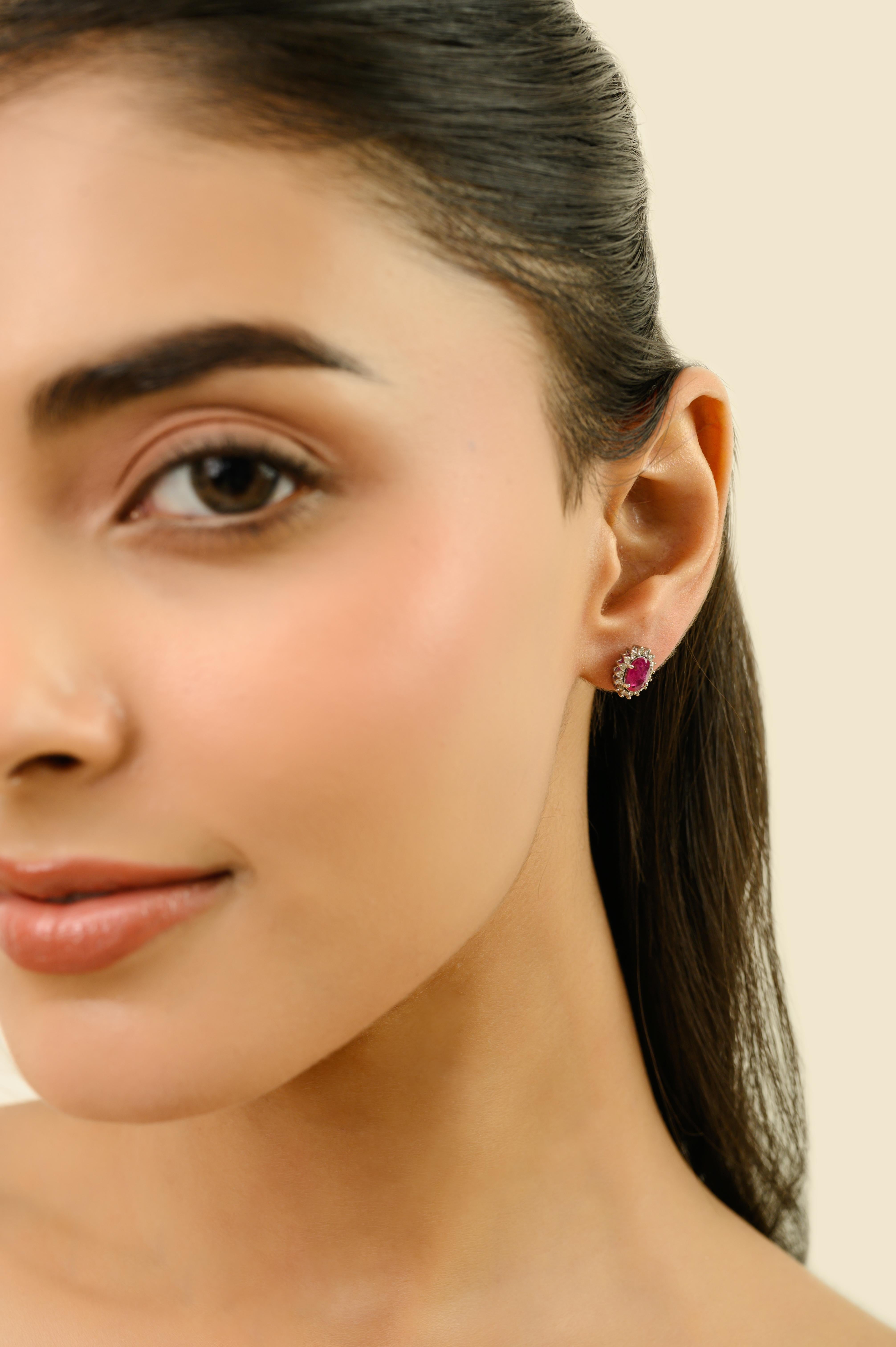 These elegant halo stud earrings feature 2 oval cut rubies totaling 1.45 carats, set in rich 18k white gold. each measuring approximately 7 x 5 mm secure with classic prong setting. Surrounding each ruby is a sparkling halo of round brilliant