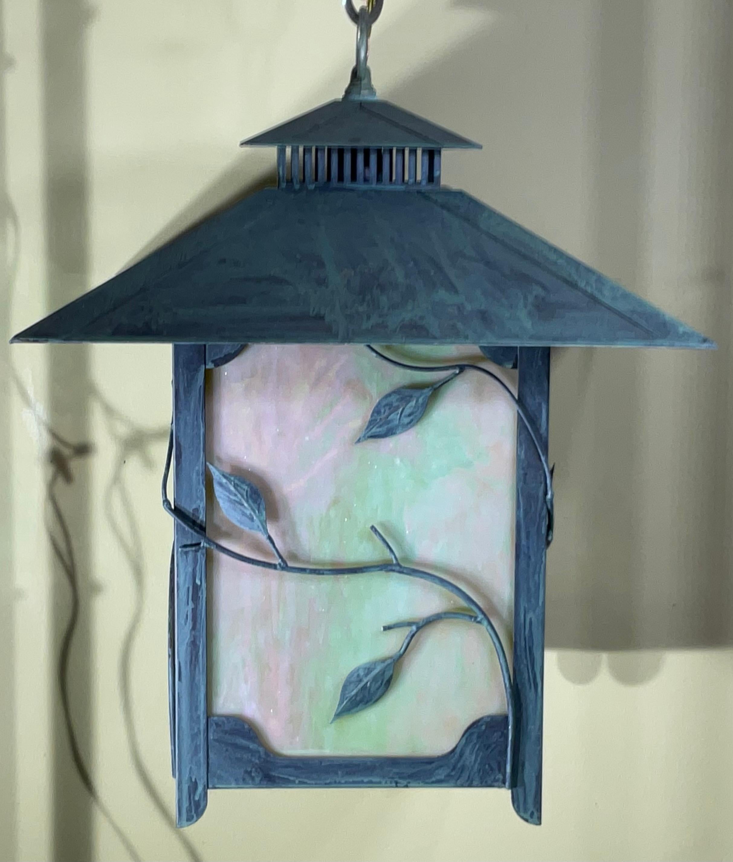 Cette lanterne exquise est une véritable œuvre d'art, alliant l'élégance du laiton massif à la beauté captivante du verre d'art. Son design complexe et sa riche patine créent une ambiance chaleureuse et accueillante, parfaite pour tout espace