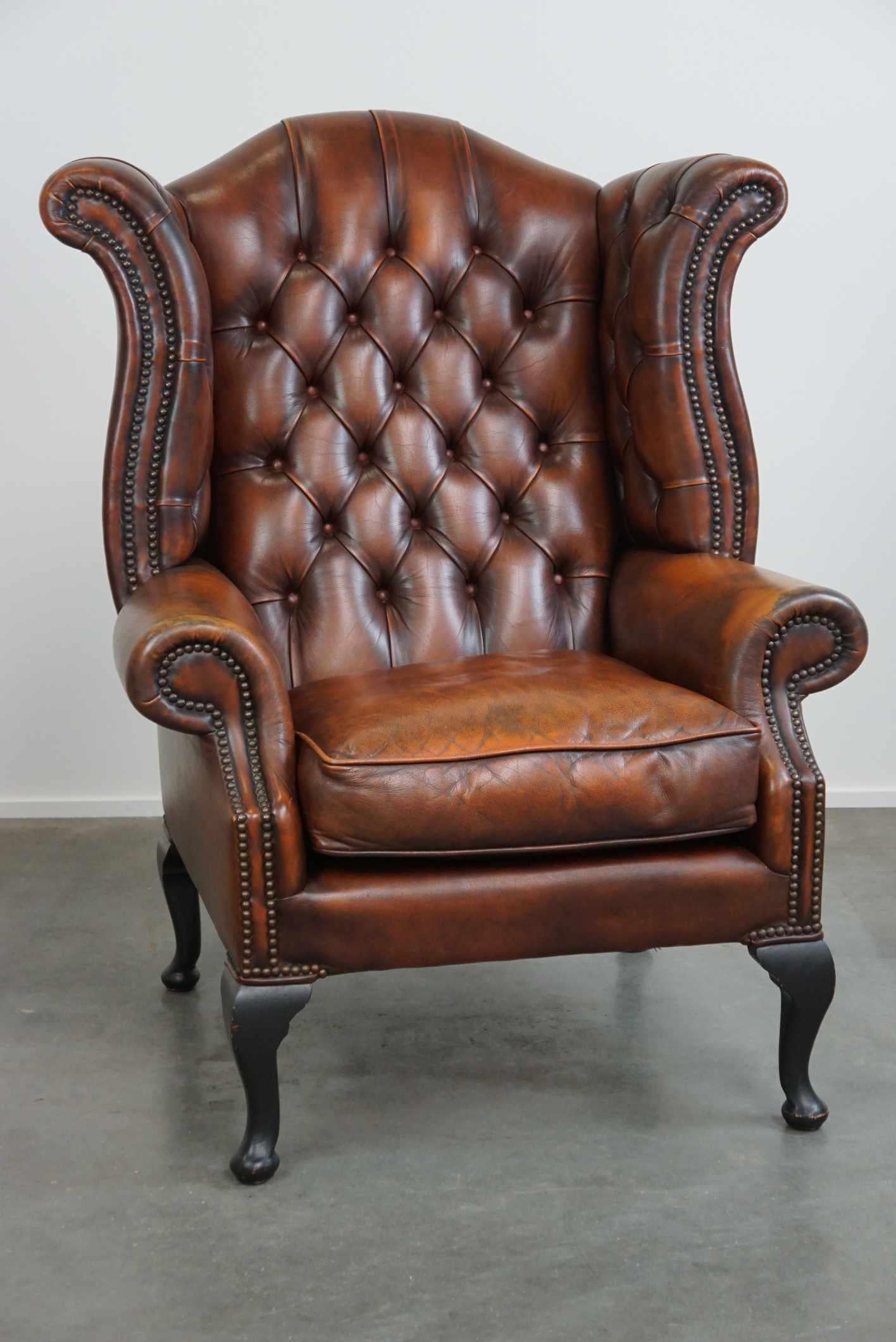 Offered: this comfortable and timeless cognac-colored English cowhide Chesterfield wingback armchair in good condition.

This beautiful cowhide wingback armchair is in good condition and provides comfortable seating. It features a detachable seat