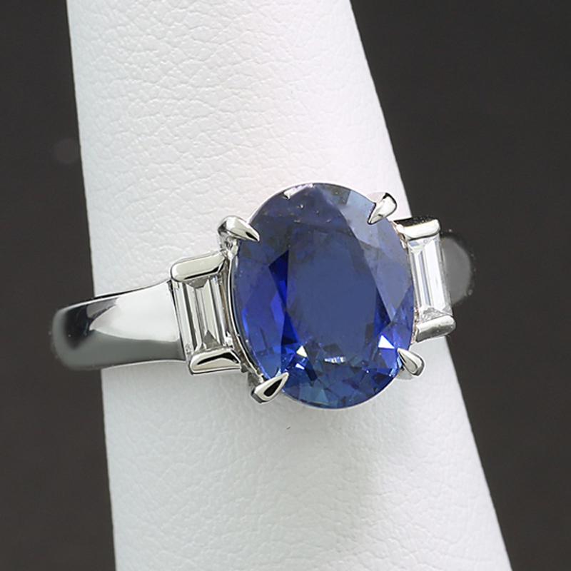 Celebrate love’s enduring journey with this exquisite trilogy-style ring, featuring a captivating 3.50-carat sapphire of exceptional transparent quality. Faceted in an elegant oval cut and set securely in a four-prong mount, the rich, deep blue hue