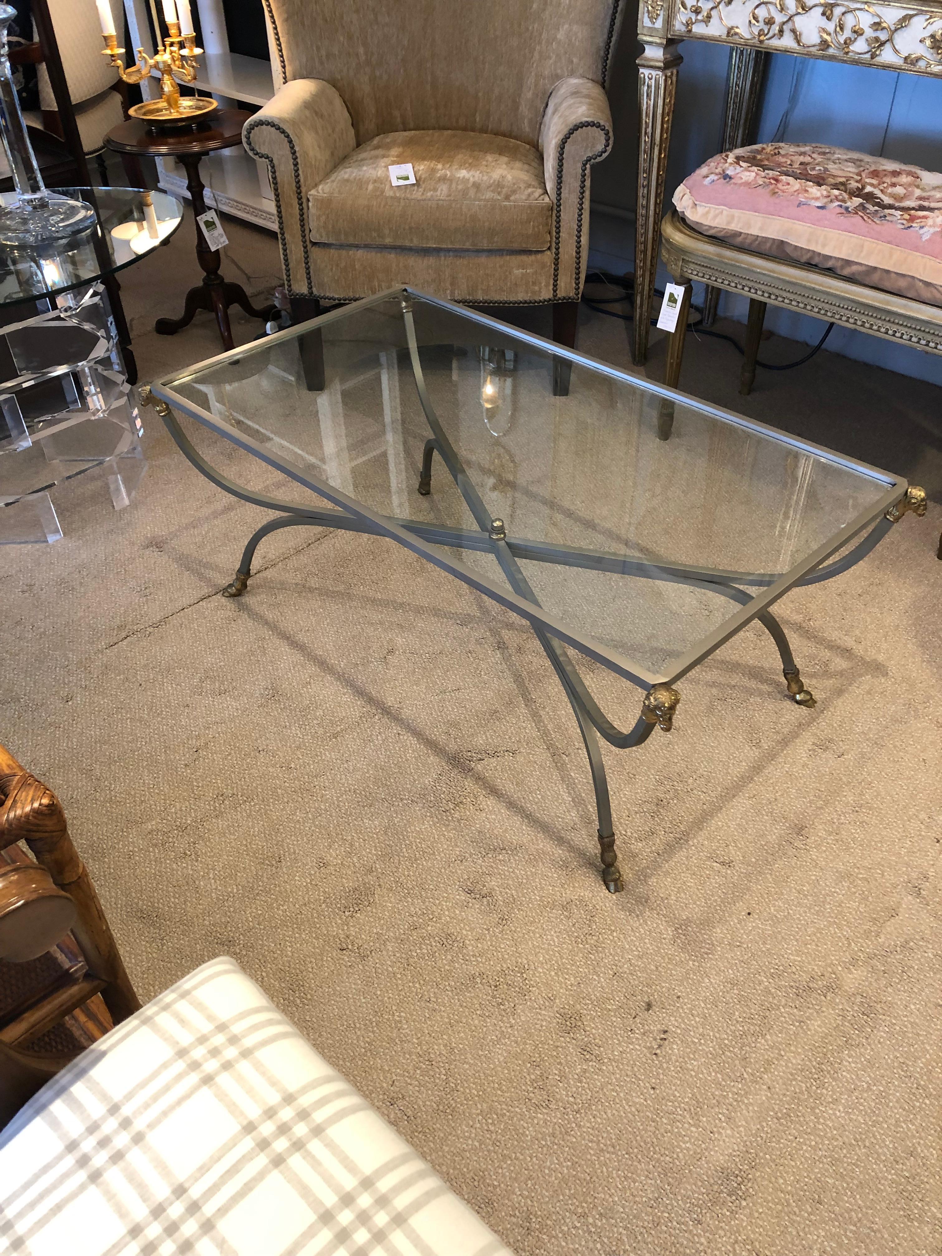 Elegant Maison Jansen style sleek sophisticated rectangular coffee table having steel frame and stylish X stretcher, embellished with the classic brass rams heads in each corner, hoof feet and central finial.