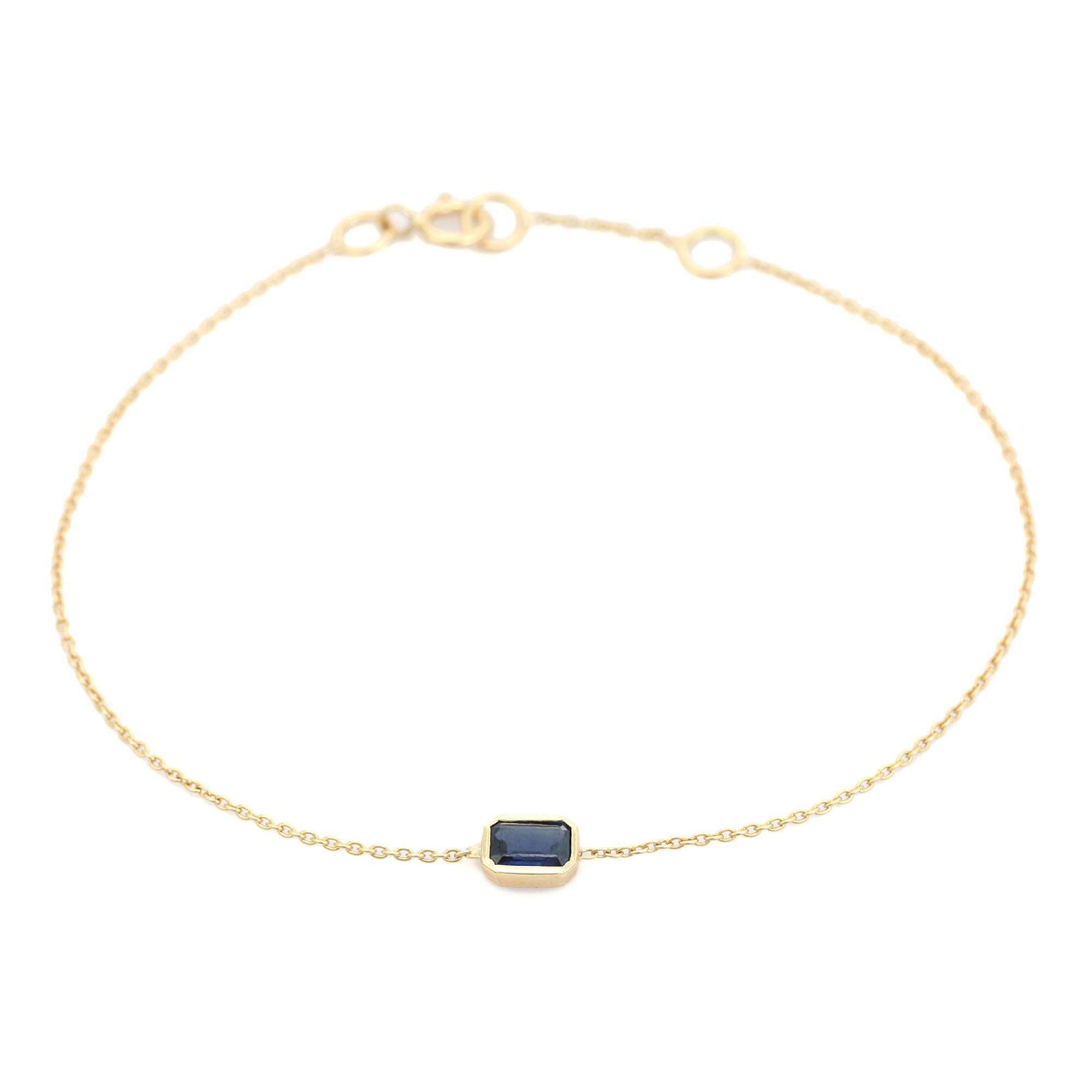  Esta pulsera lleva un zafiro azul talla esmeralda de 0,36 ct en engaste biselado, elaborado en oro amarillo de 14 quilates. El zafiro está firmemente enmarcado en oro liso, lo que permite que destaque su profundo tono azul. Engarzada en una fina