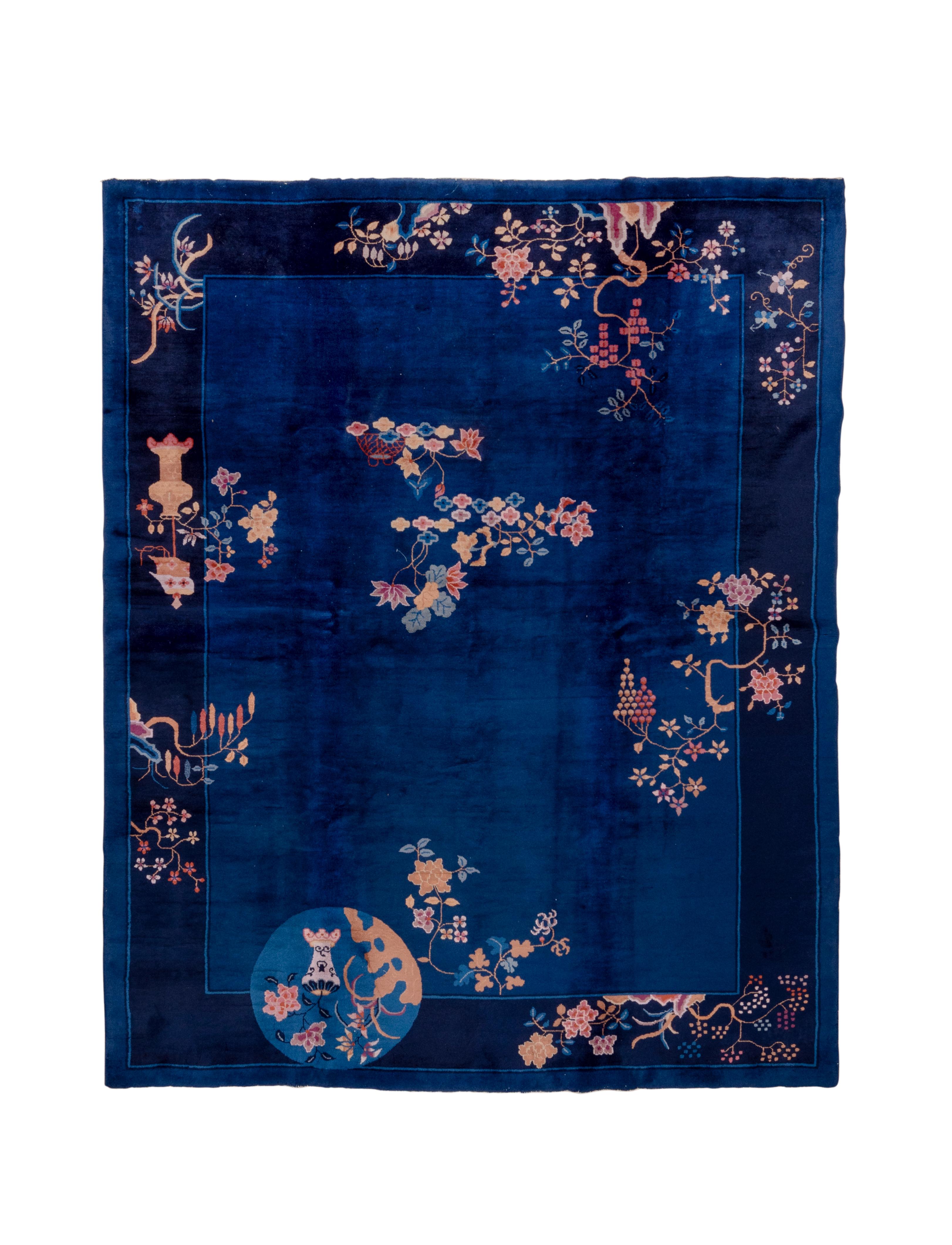 The royal blue field is framed by the navy border from which grow into the field writhing stems and grape bunches, along with vases and a medium blue disc with another vase.  Off centre  blossoms and stalks adorn the field. A very striking rug with