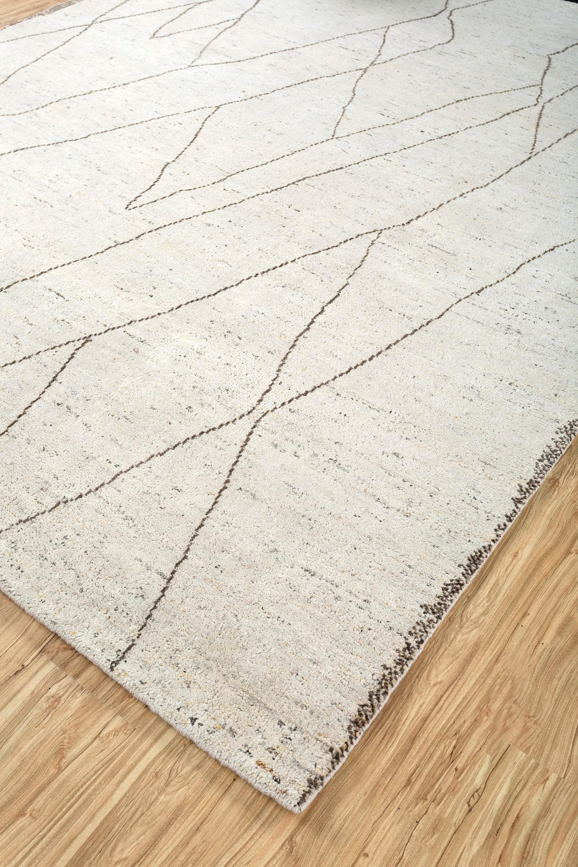 Ce tapis en laine nouée à la main, fabriqué dans l'Inde rurale, réimagine des motifs intemporels avec une touche indéniablement contemporaine. Le riche fond blanc naturel devient une toile pour une tapisserie éclectique de formes géométriques, dont
