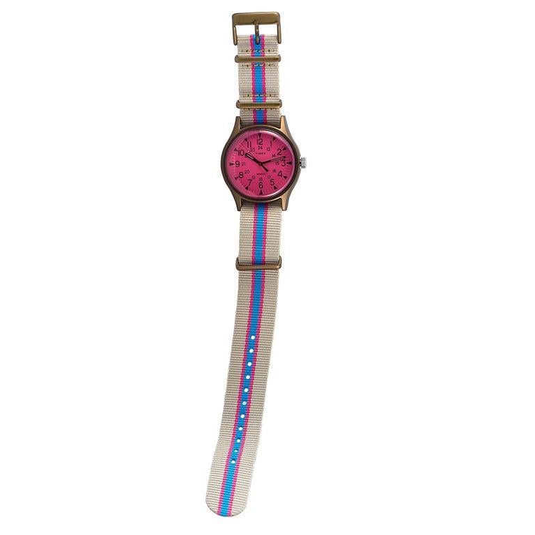 This is the Timex MK1 Aluminum California 40 mm, reference number TW2T25600. The watch boasts an aluminum case that is fitted with a stainless steel back and measures 40 mm in diameter. The pink dial with Arabic numerals features central hours,