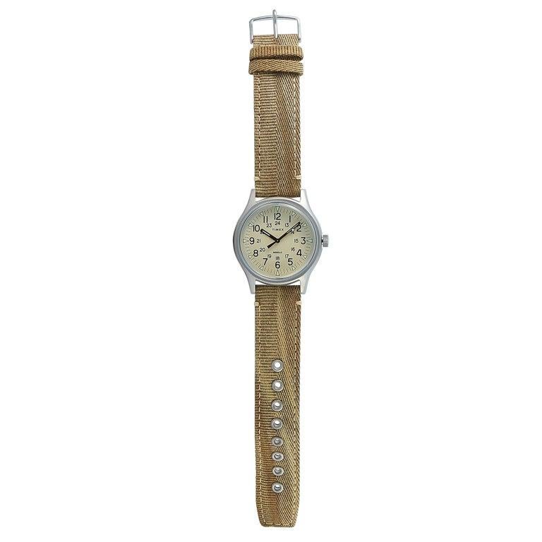 This is the Timex MK1 40 mm watch, reference number TW2R68000. It is presented with a stainless steel case that offers water resistance of 30 meters. The case measures 40 mm in diameter and is mounted onto a beige khaki fabric strap, secured on the