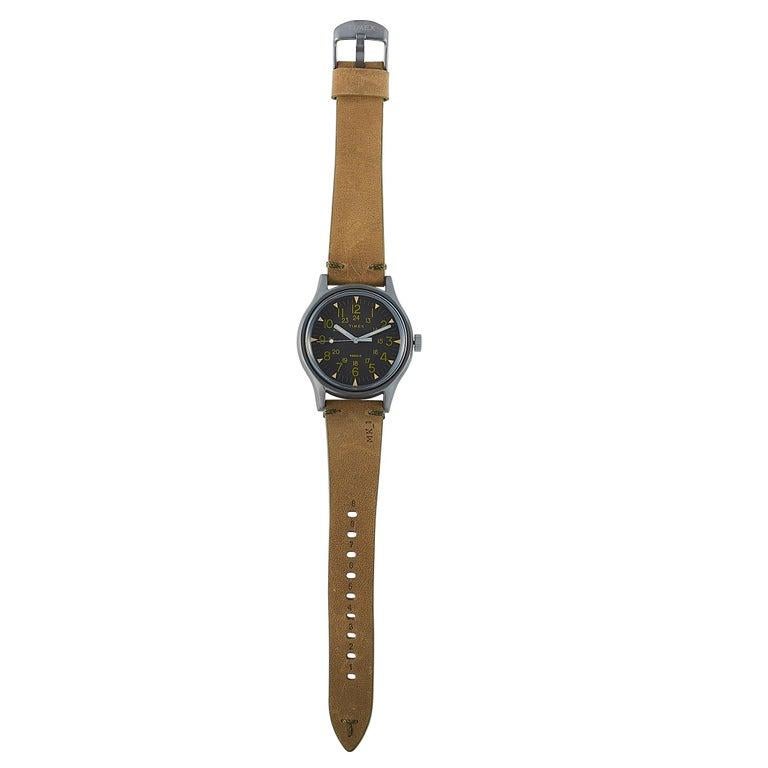 Dies ist die Timex MK1 40 mm, Referenznummer TW2R97000. Die Uhr wird mit einem Edelstahlgehäuse mit einem Durchmesser von 40 mm präsentiert. Das Gehäuse ist bis zu 30 Meter wasserdicht und wird an einem braunen Lederarmband mit Dornschließe