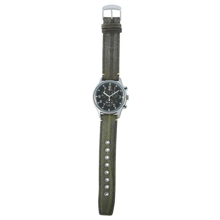 This is the Timex MK1 Steel Chronograph 42 mm watch, reference number TW2R68600. It is presented with a stainless steel case that offers water resistance of 50 meters. The case measures 42 mm in diameter and is mounted onto an olive green fabric
