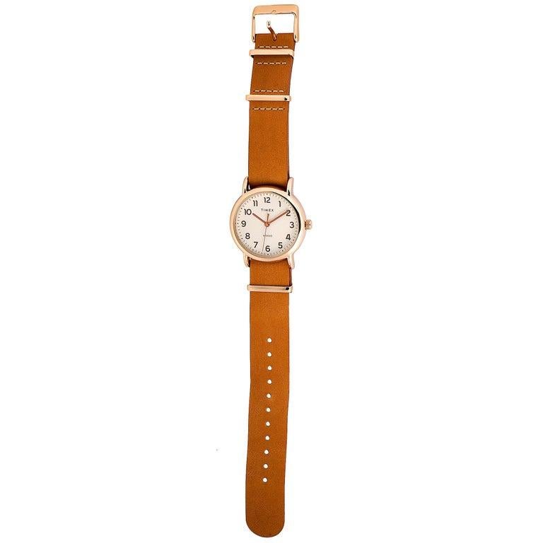 This is the Timex Weekender 38 mm, reference number TW2R59600-A. The watch is presented with a 38 mm rose gold-tone low lead brass case that boasts stainless steel back. The case offers water resistance of 30 meters and is mounted onto a brown