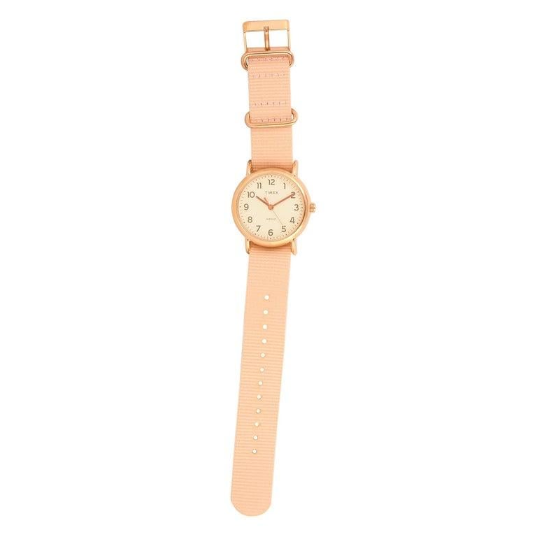 This is the Timex Weekender 38 mm, reference number TW2R59600. The watch is presented with a 38 mm rose gold-tone low lead brass case that boasts stainless steel back. The case offers water resistance of 30 meters and is mounted onto a blush fabric