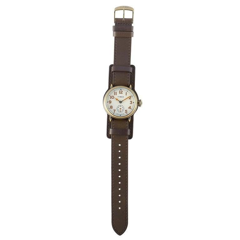 This is the Timex Welton 38 mm, reference number TW2R87900, inspired by the first Timex wristwatch. The watch is presented with a 38 mm stainless steel case that boasts an antique bronze finish. The cream dial with Arabic numerals features central