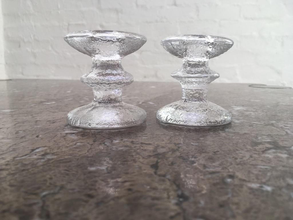 Pair of candlesticks by Timo Sarpaneva. One with remnant Iittala label. The other signed 'TS'. 

First produced in 1967 and remained very popular throughout the 1970s. A classic table decoration with exquisite ice-like clarity. 

No two of these