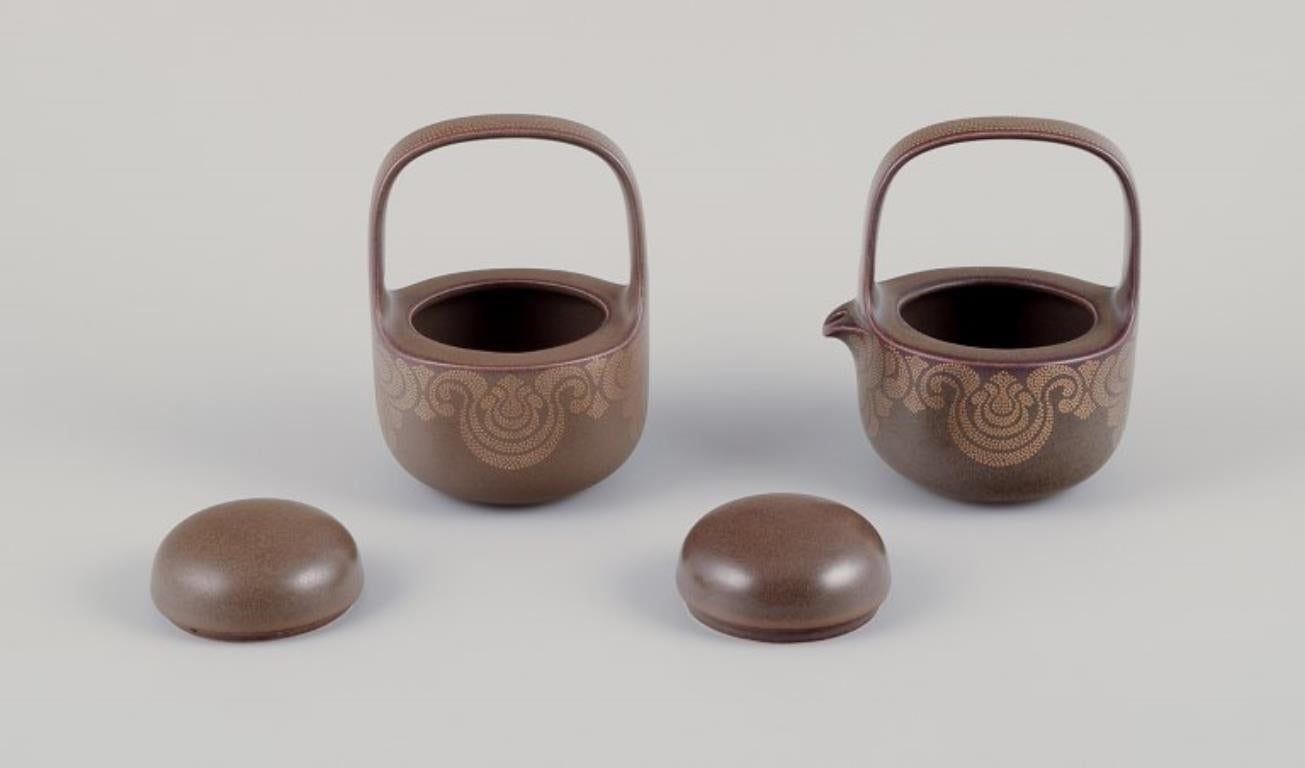 Timo Sarpaneva für Rosenthal. Porzellancreme- und Zuckerschale „Kaari“ aus Porzellan.
Braune Glasur mit Goldverzierung.
1980s.
Markiert.
In perfektem Zustand. Erscheint wie neu.
Milchkännchen: H 13,0 cm x T 10,0 cm.
Zuckerdose: H 13,0 cm x T 9,5 cm.