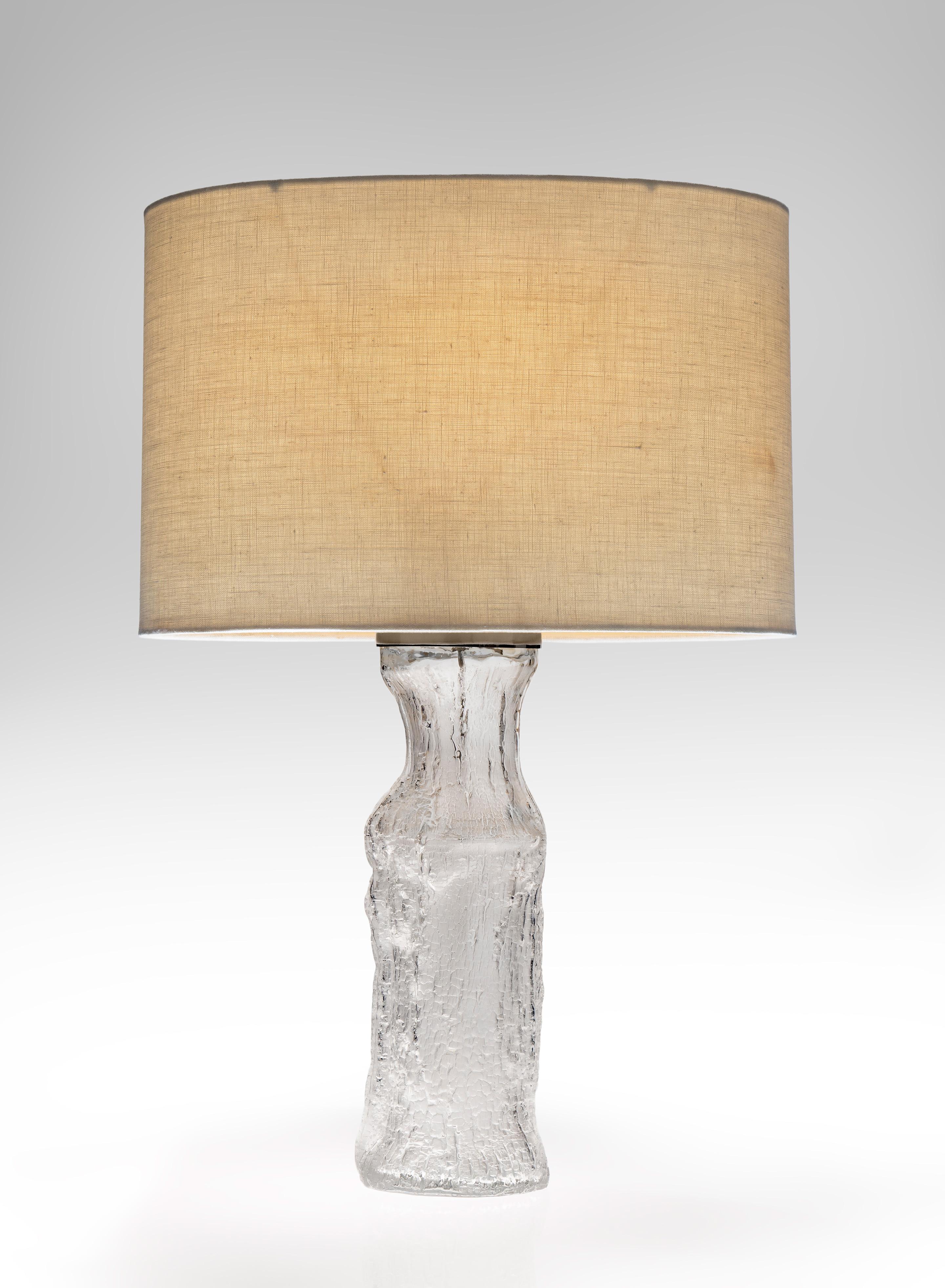 The textured bottle shape formed by hand blowing glass into a charred wood mold which produced individual lamps, each unique. The Swedish firm, Luxus under and exclusive contract, made the Ittala glass into lamps. Now wired for American use with a